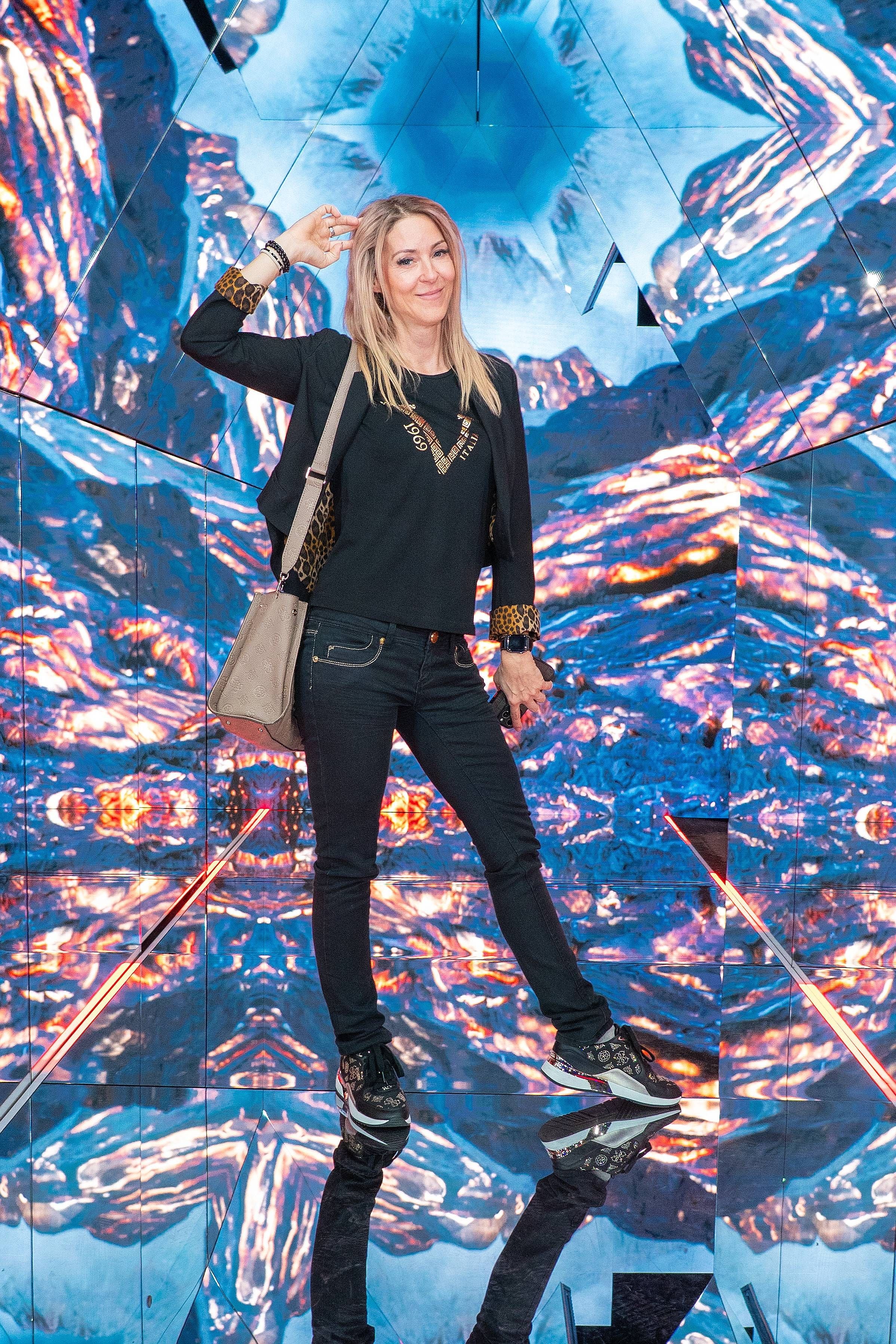 Frau steht lächelnd vor einem bunten, kaleidoskopartigen Hintergrund im Immersium Wien.