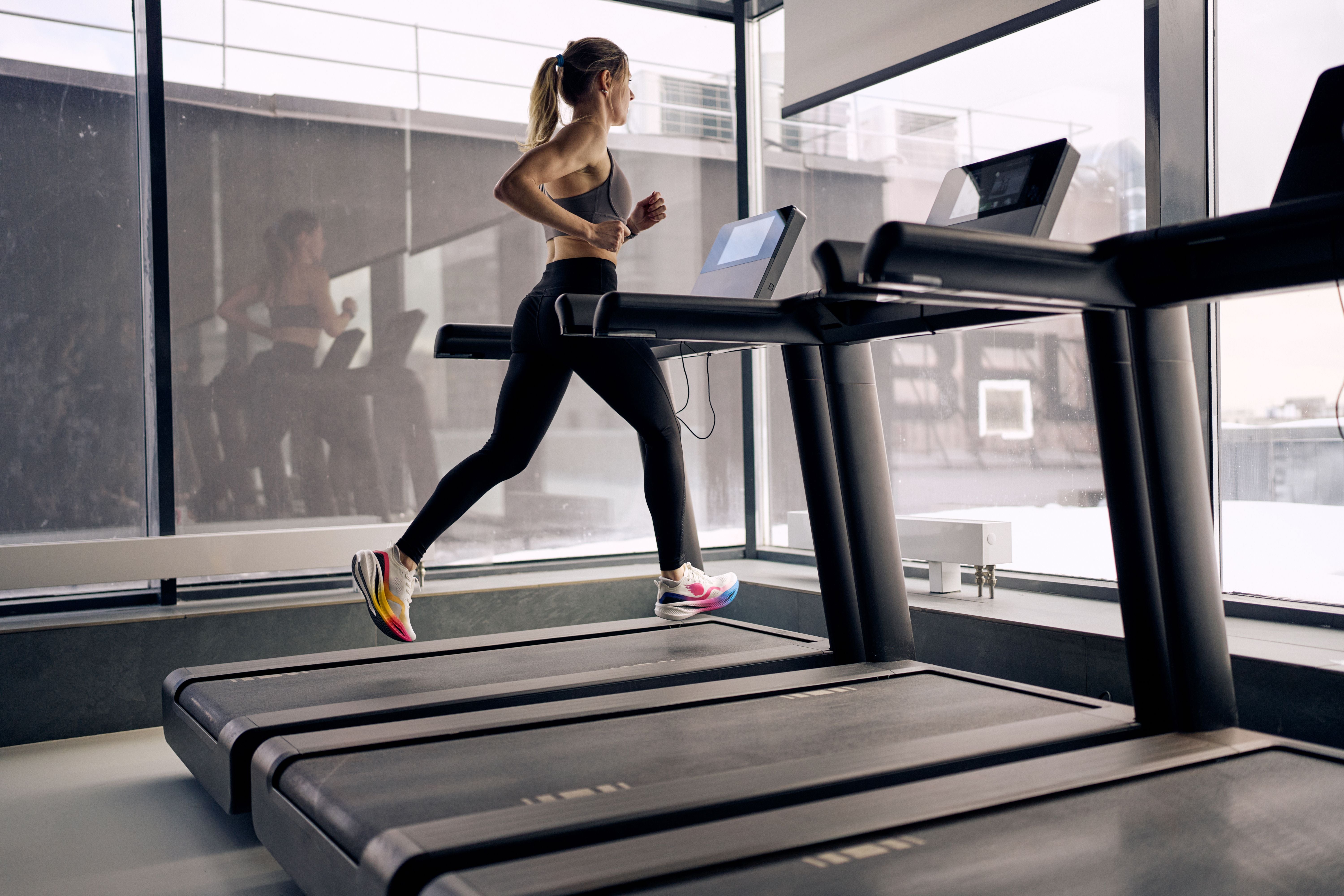 Junge Frau läuft fokussiert auf einem Laufband in einem hellen Fitnessstudio.