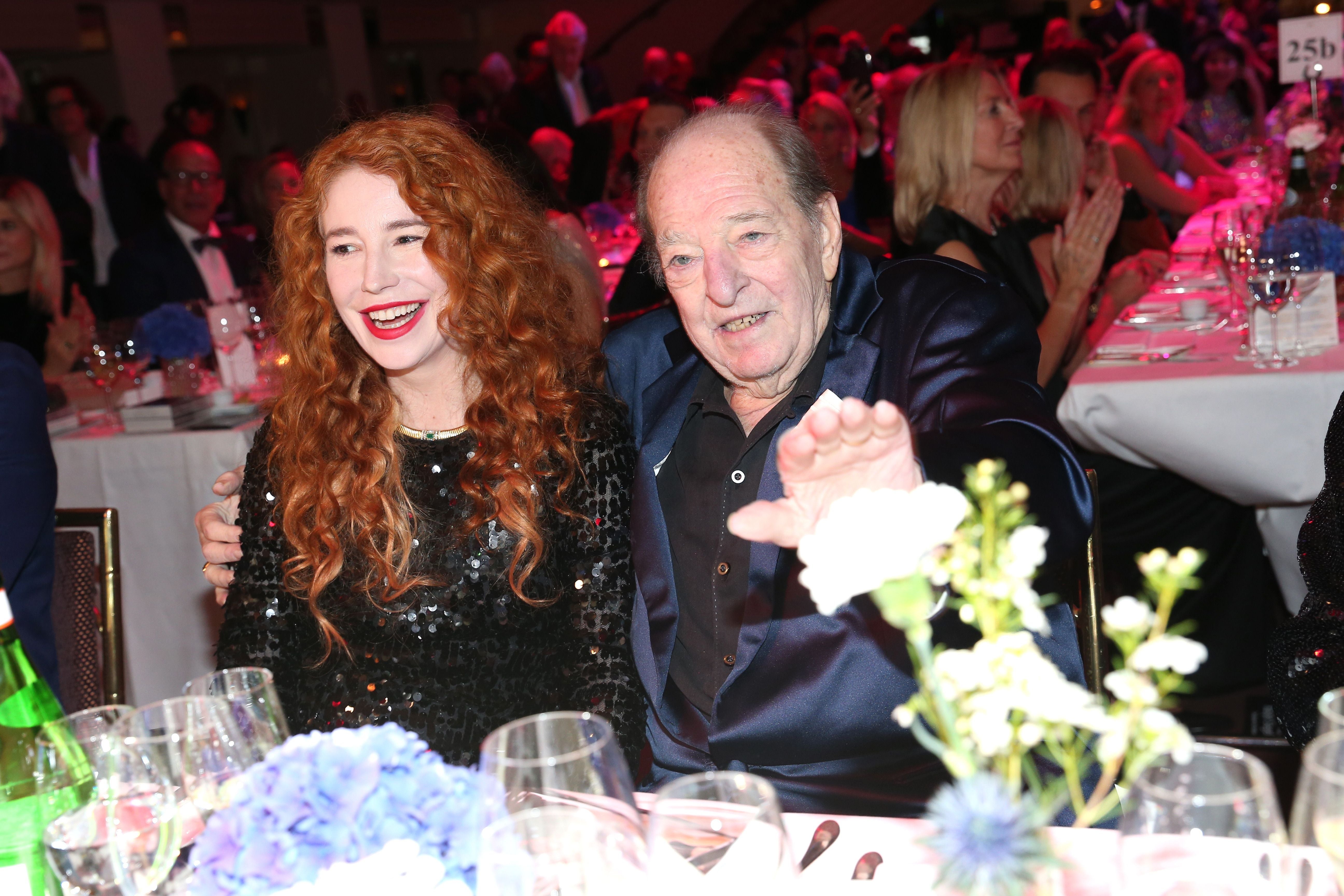 Ein Mann und eine Frau lachen an einem festlich gedeckten Tisch bei einer Gala.