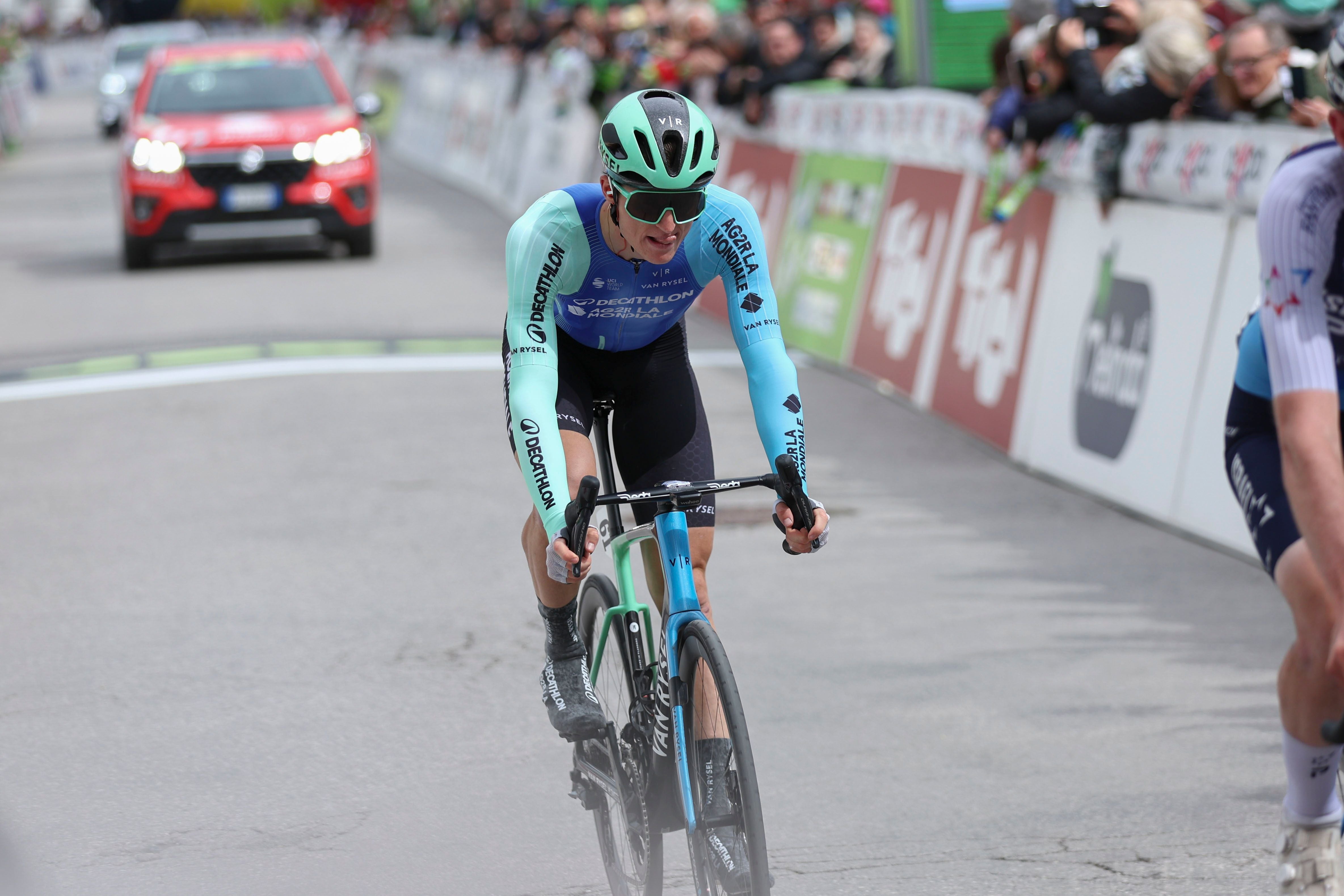 Radrennfahrer mit blauem Trikot fährt beim Zieleinlauf eines Rennens, Zuschauer im Hintergrund.