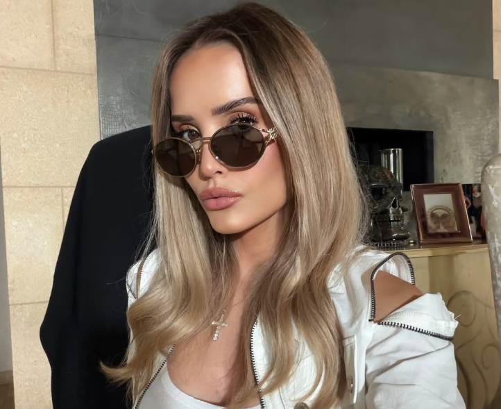 Frau mit langen blonden Haaren und Sonnenbrille posiert für ein Selfie.