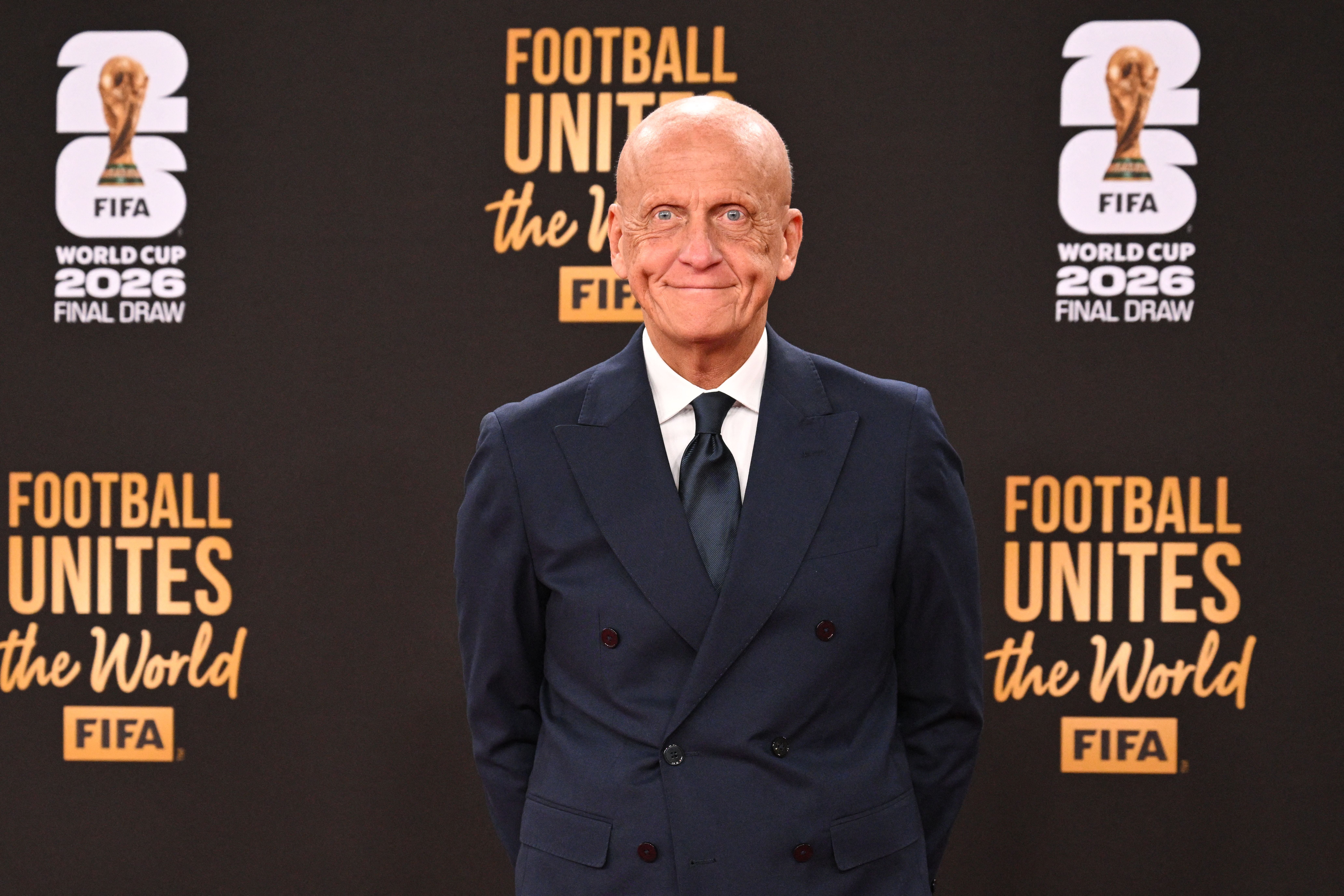 Ein Mann im Anzug steht lächelnd vor einer FIFA World Cup 2026 Fotowand.