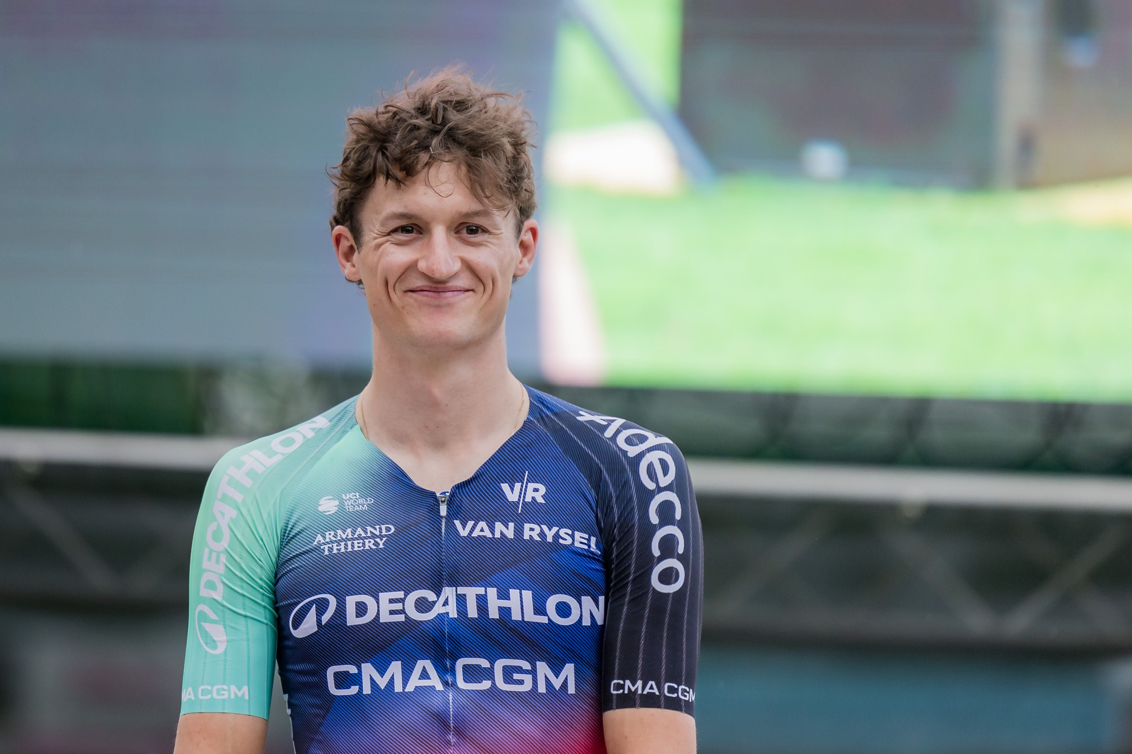 Ein junger Mann im Decathlon-Radtrikot lächelt in die Kamera.