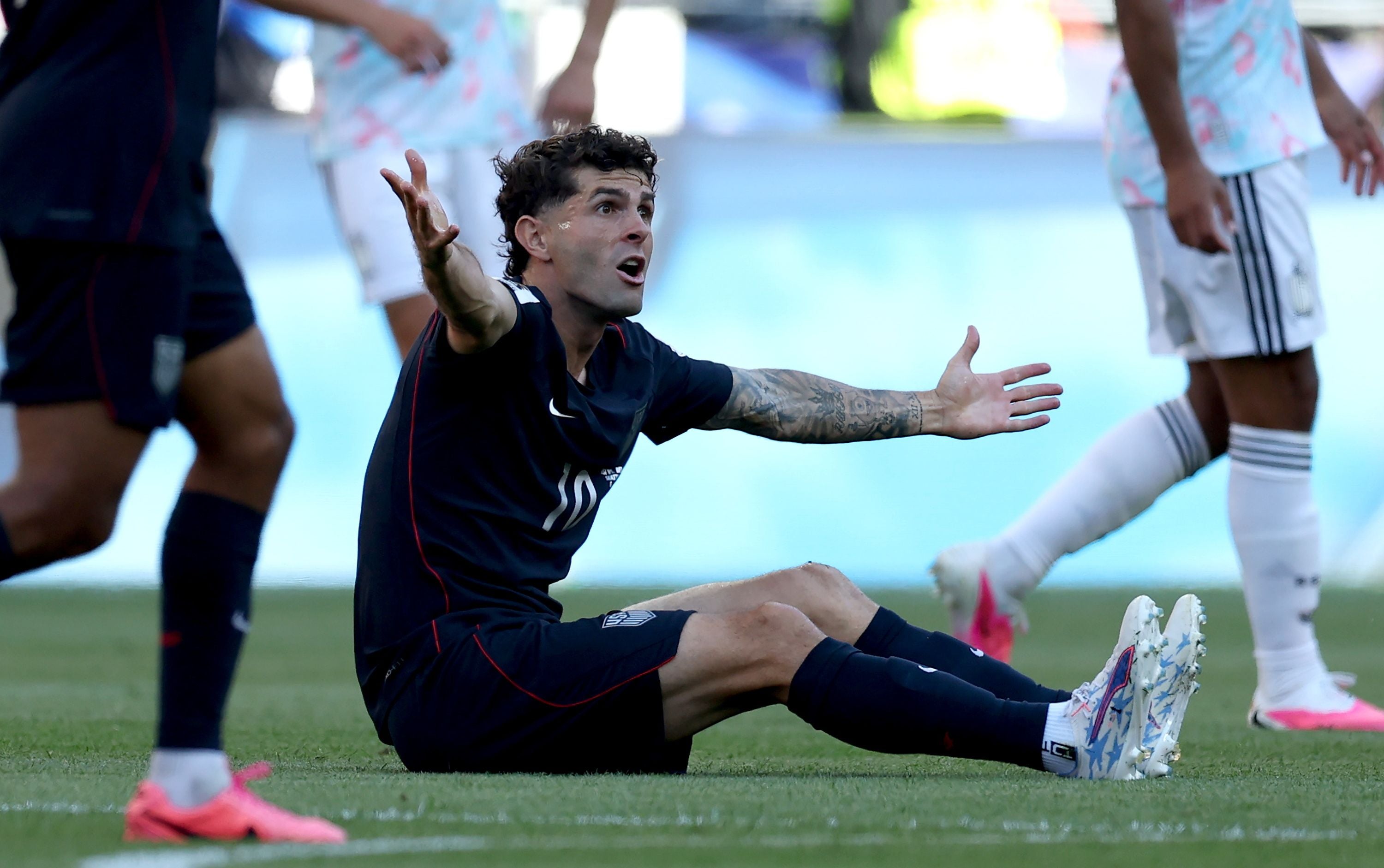 Ein US-Spieler sitzt auf dem Rasen und gestikuliert mit ausgebreiteten Armen während eines Fußballspiels.