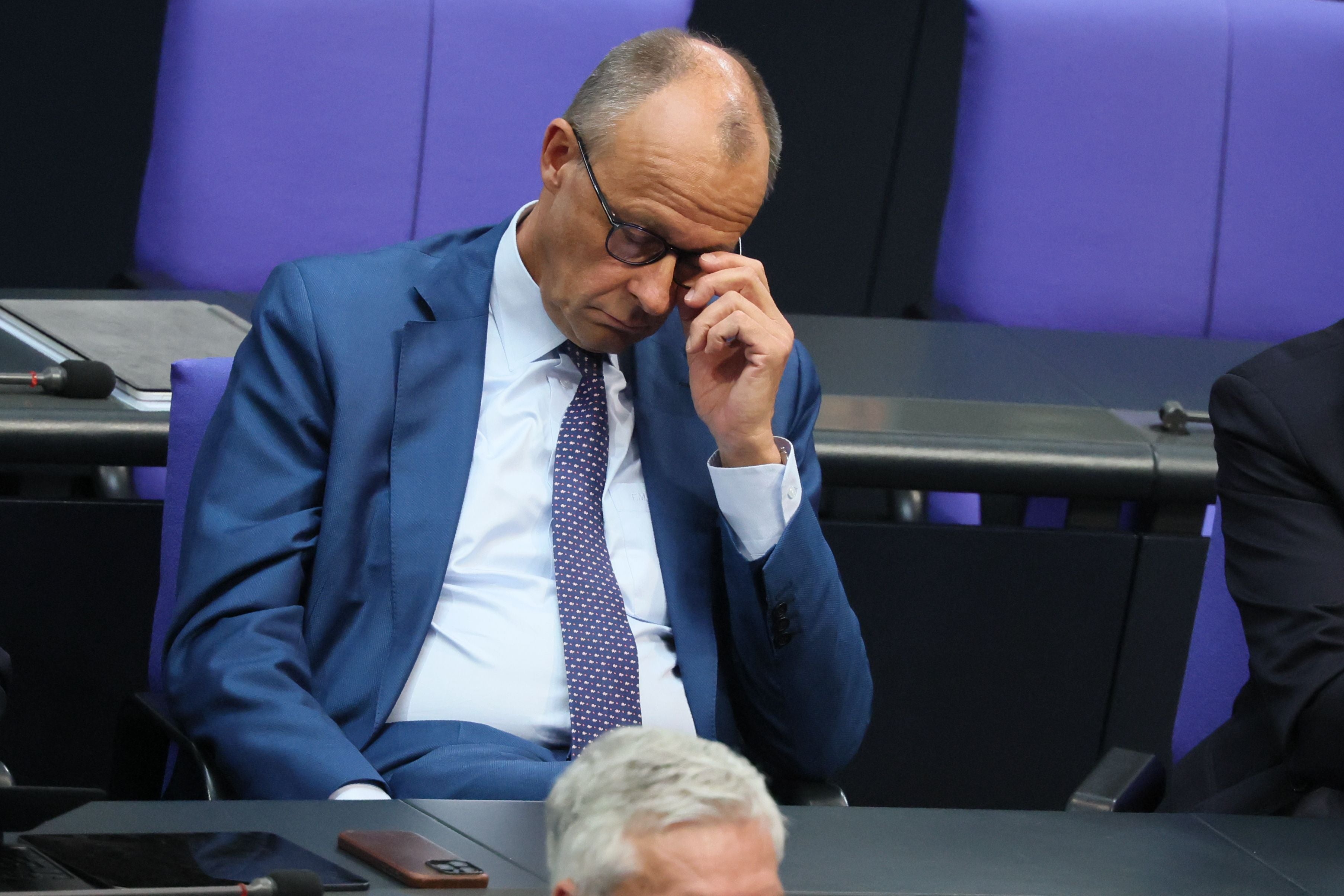 Ein Mann im blauen Anzug sitzt nachdenklich mit geschlossenen Augen im Parlament.