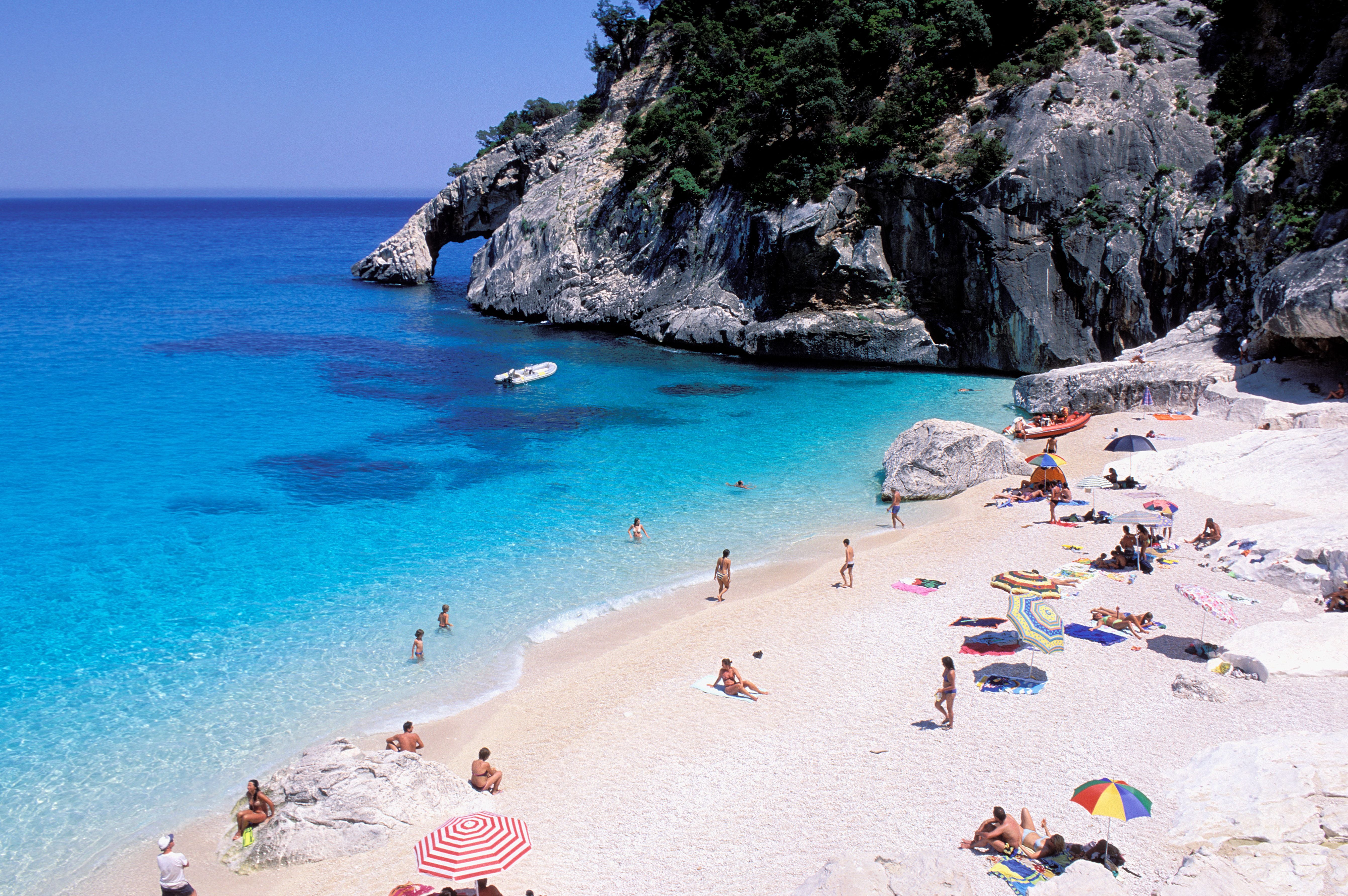 Strand mit bunten Sonnenschirmen, türkisblauem Wasser und Felsen bei Cala Goloritzé, Sardinien.