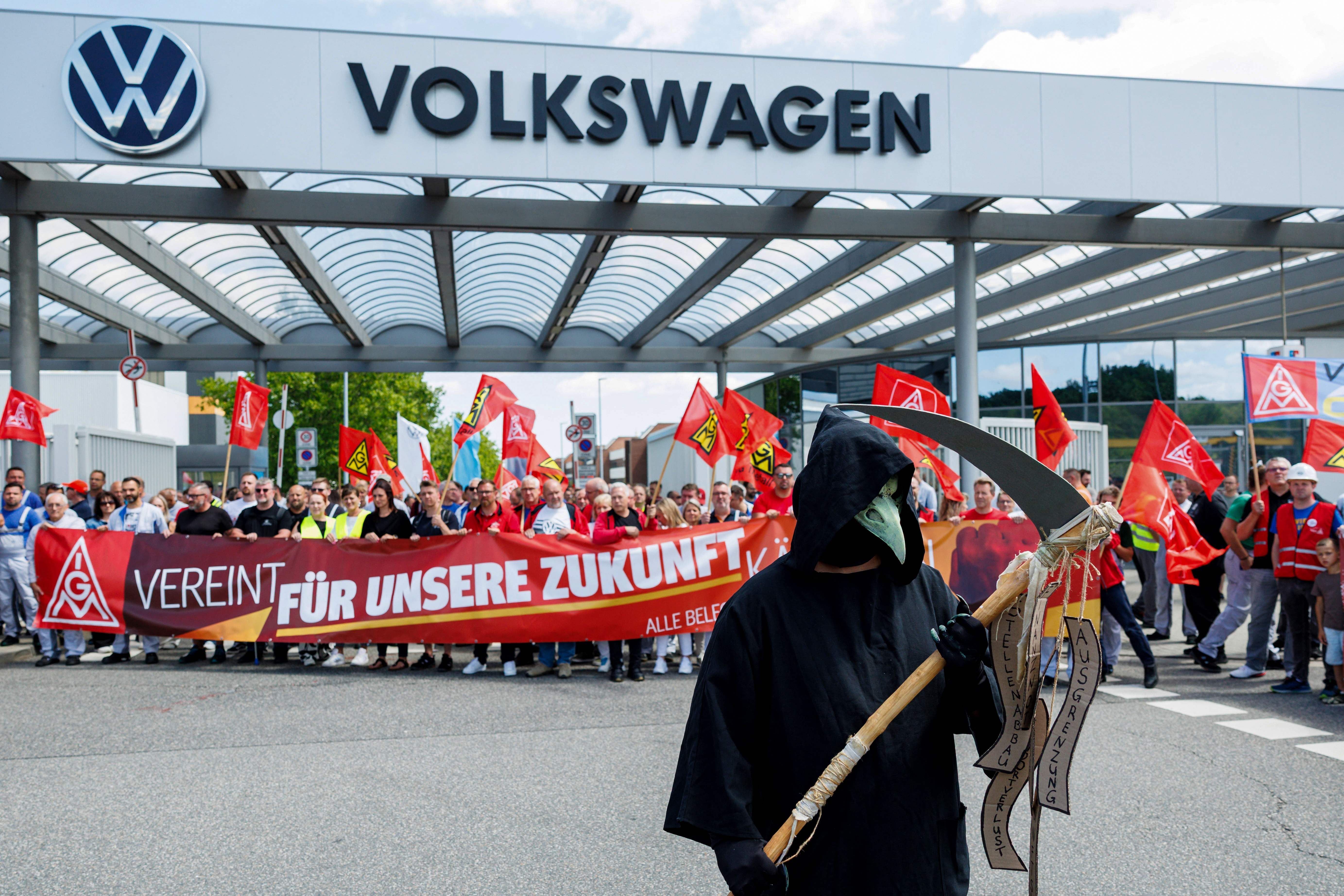 Demonstrierende VW-Mitarbeiter mit IG Metall Fahnen und Sensenmann-Kostüm vor dem Werkseingang.