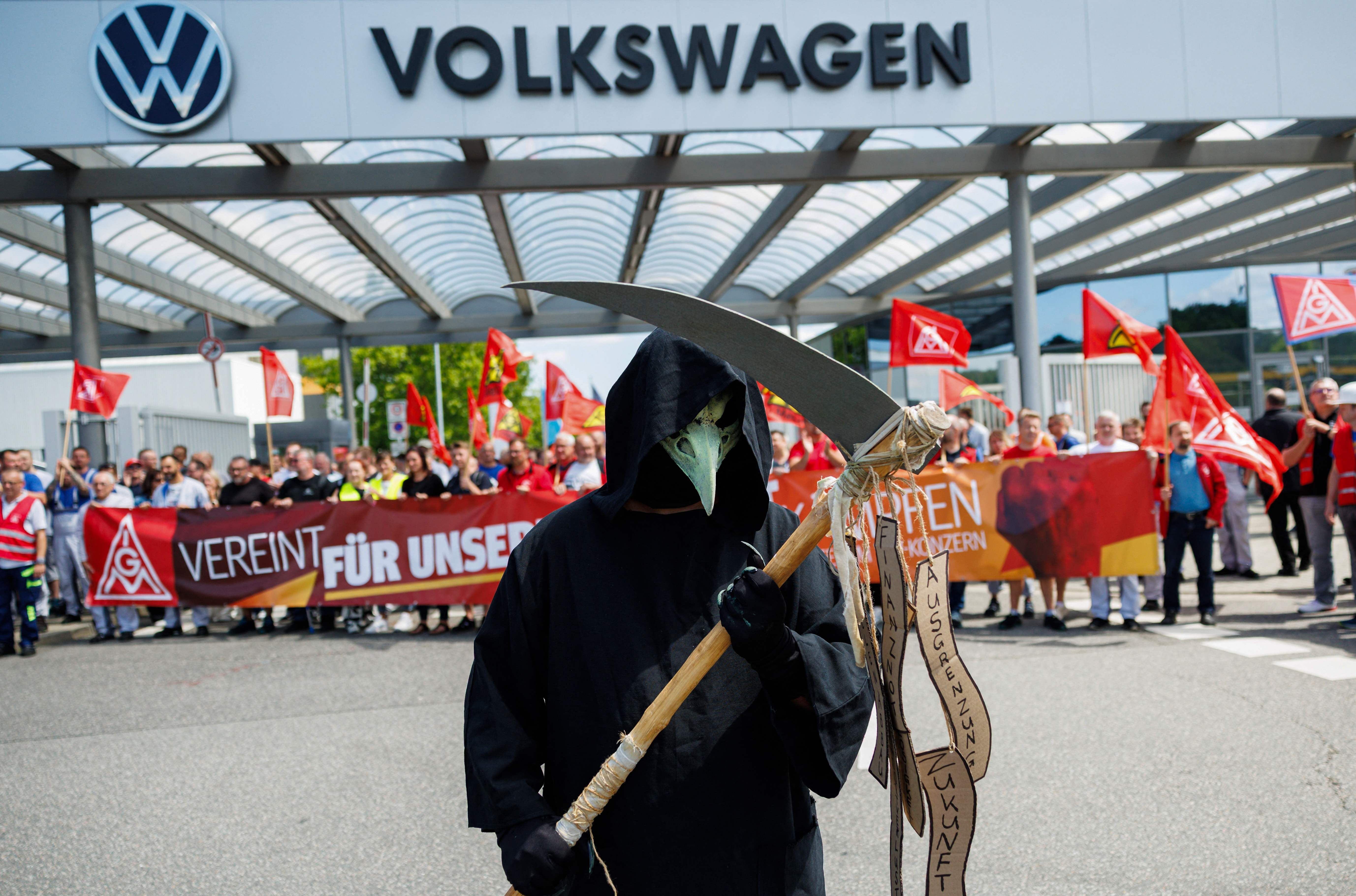 Ein als Sensenmann verkleideter Demonstrant vor VW-Werk, Streik von IG Metall und VW-Mitarbeitern im Hintergrund.