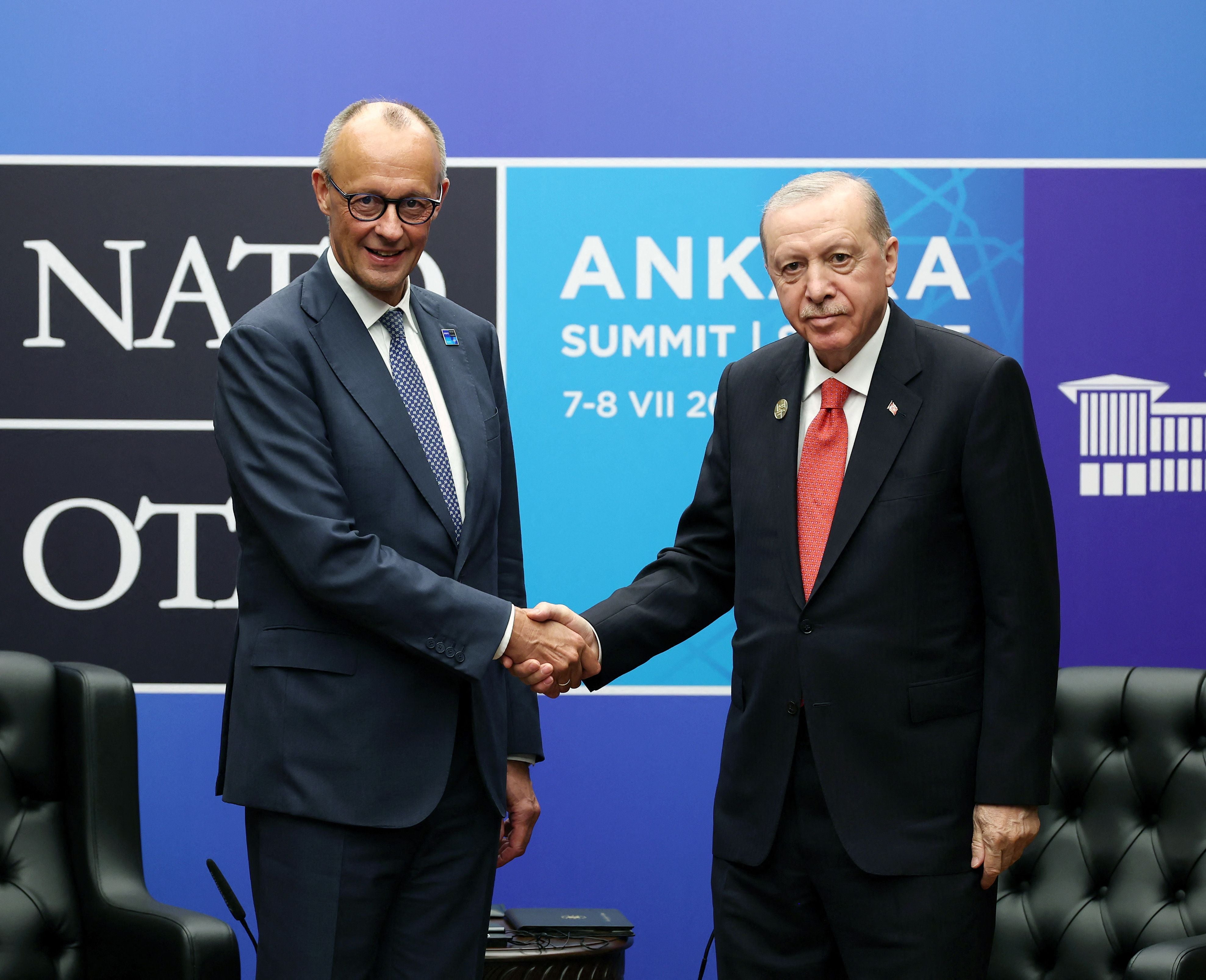 Zwei Männer im Anzug geben sich bei einem NATO-Gipfel in Ankara vor blauem Hintergrund die Hand.