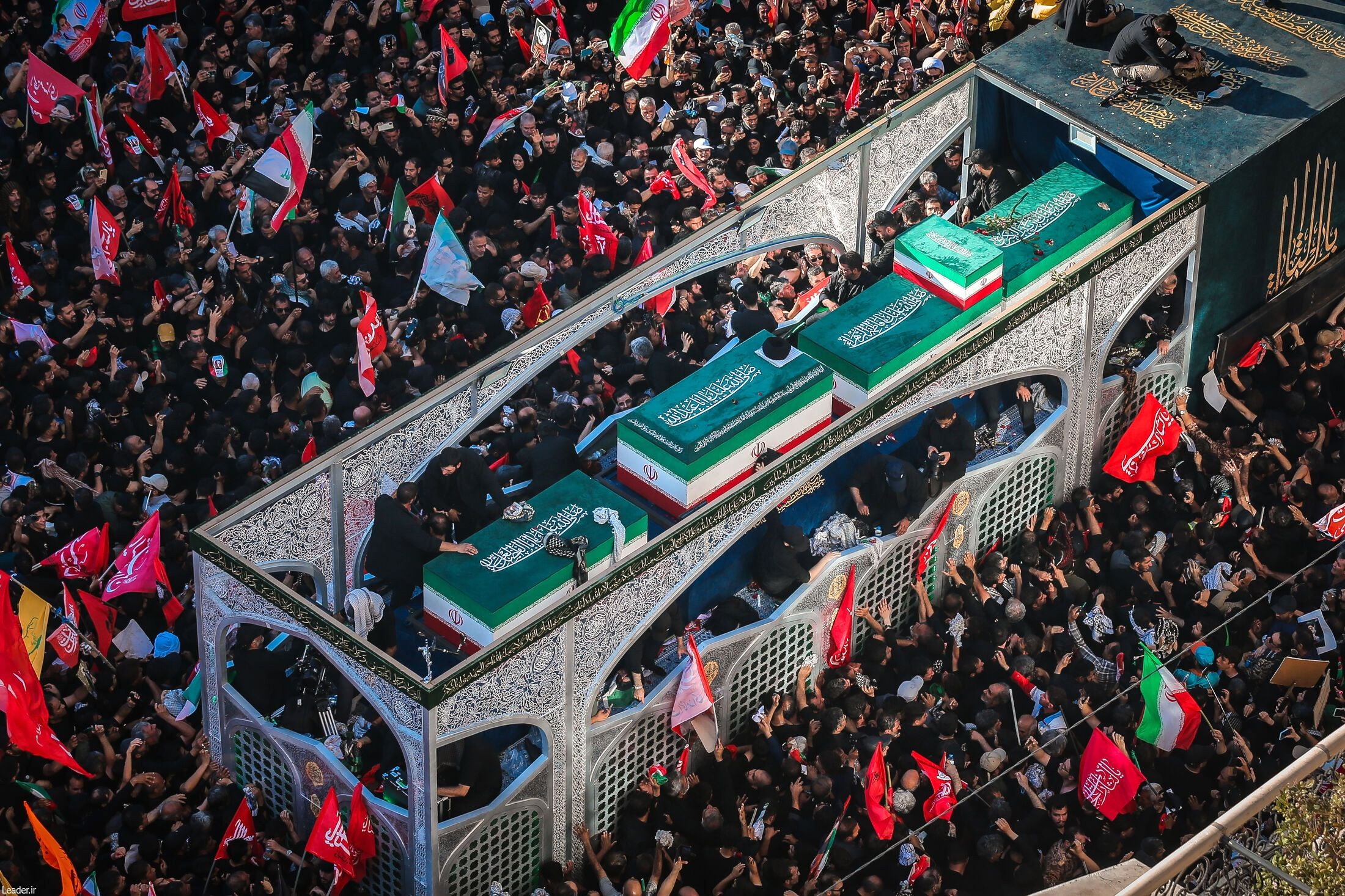 Menschenmenge bei einer Trauerprozession mit Särgen und iranischen Flaggen in Mashhad, Iran.