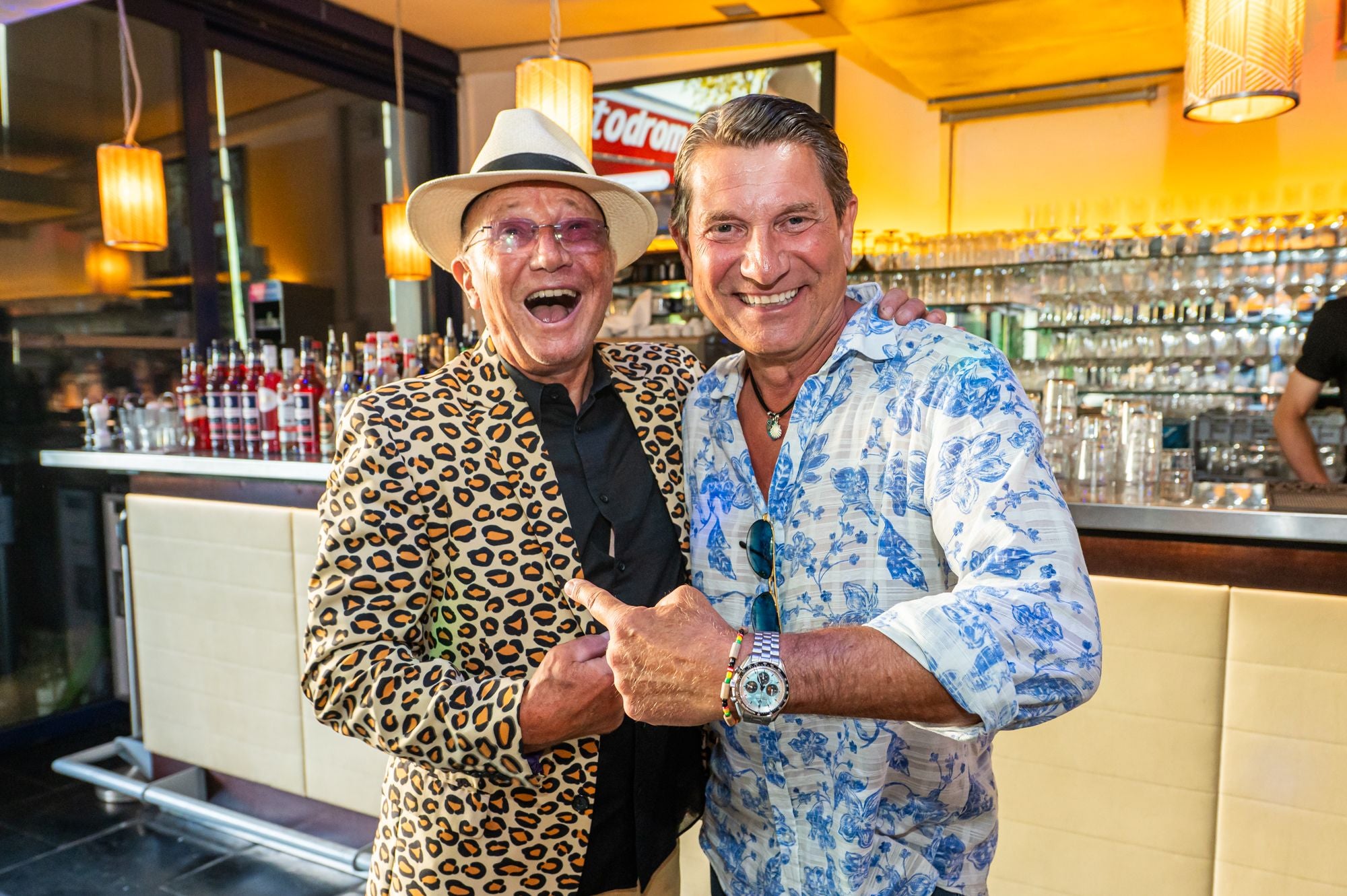 Zwei fröhliche Männer posieren lachend in einer Bar bei einer Sommerfest-Veranstaltung.