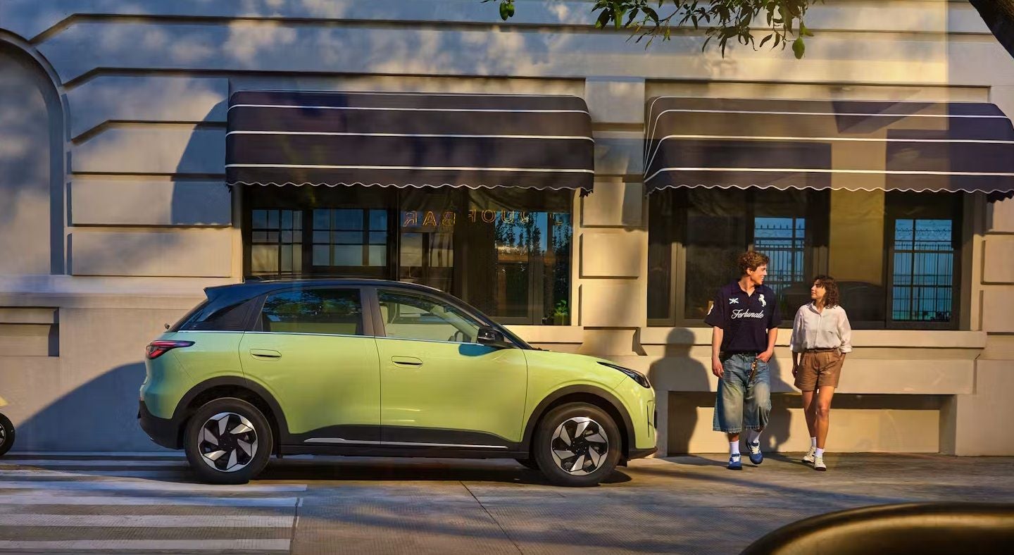 Ein grüner Geely SUV parkt an einer Straße, zwei Personen gehen auf dem Gehweg vorbei.