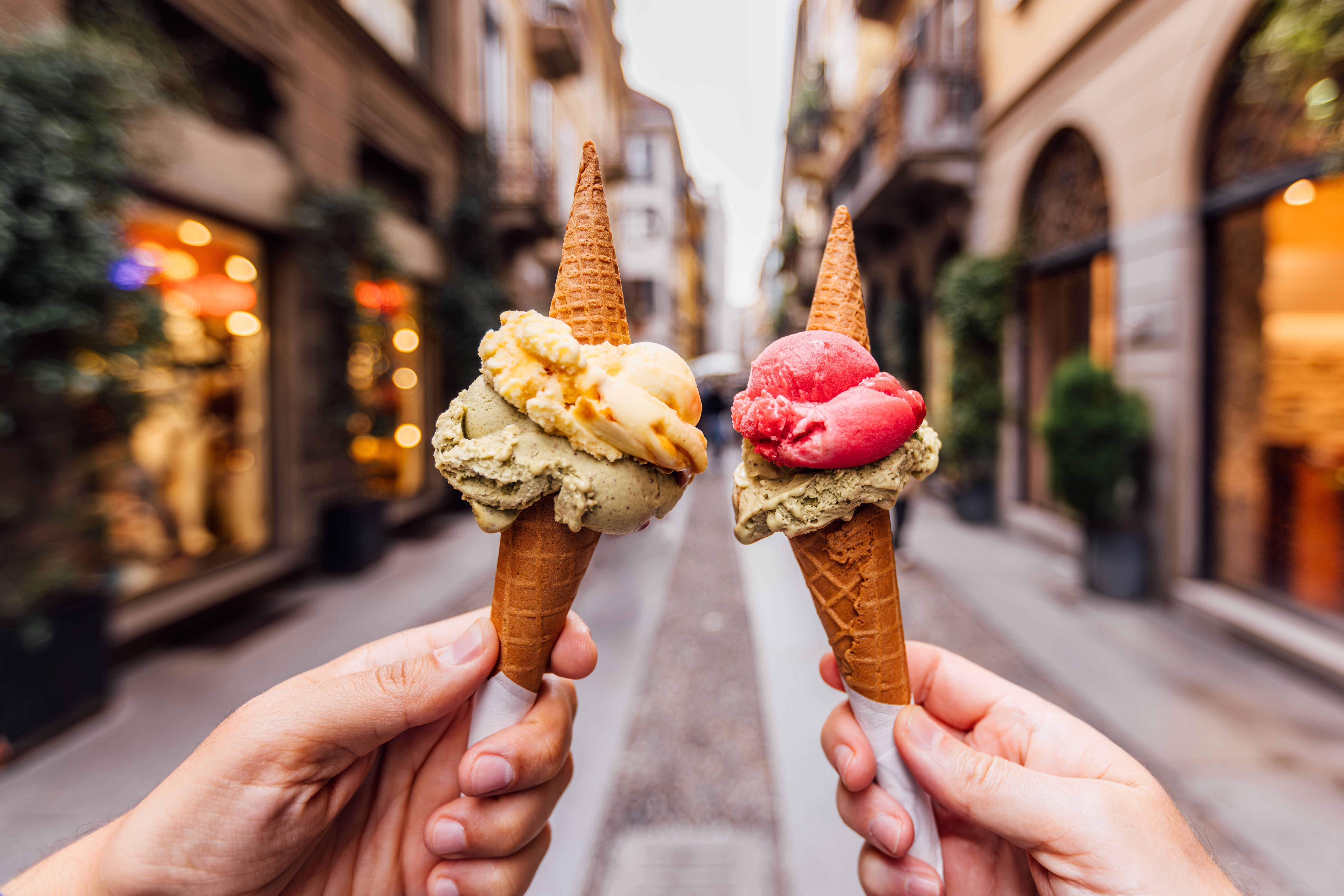 Zwei Personen halten Eiswaffeln mit verschiedenfarbigem Eis in einer Altstadtstraße.