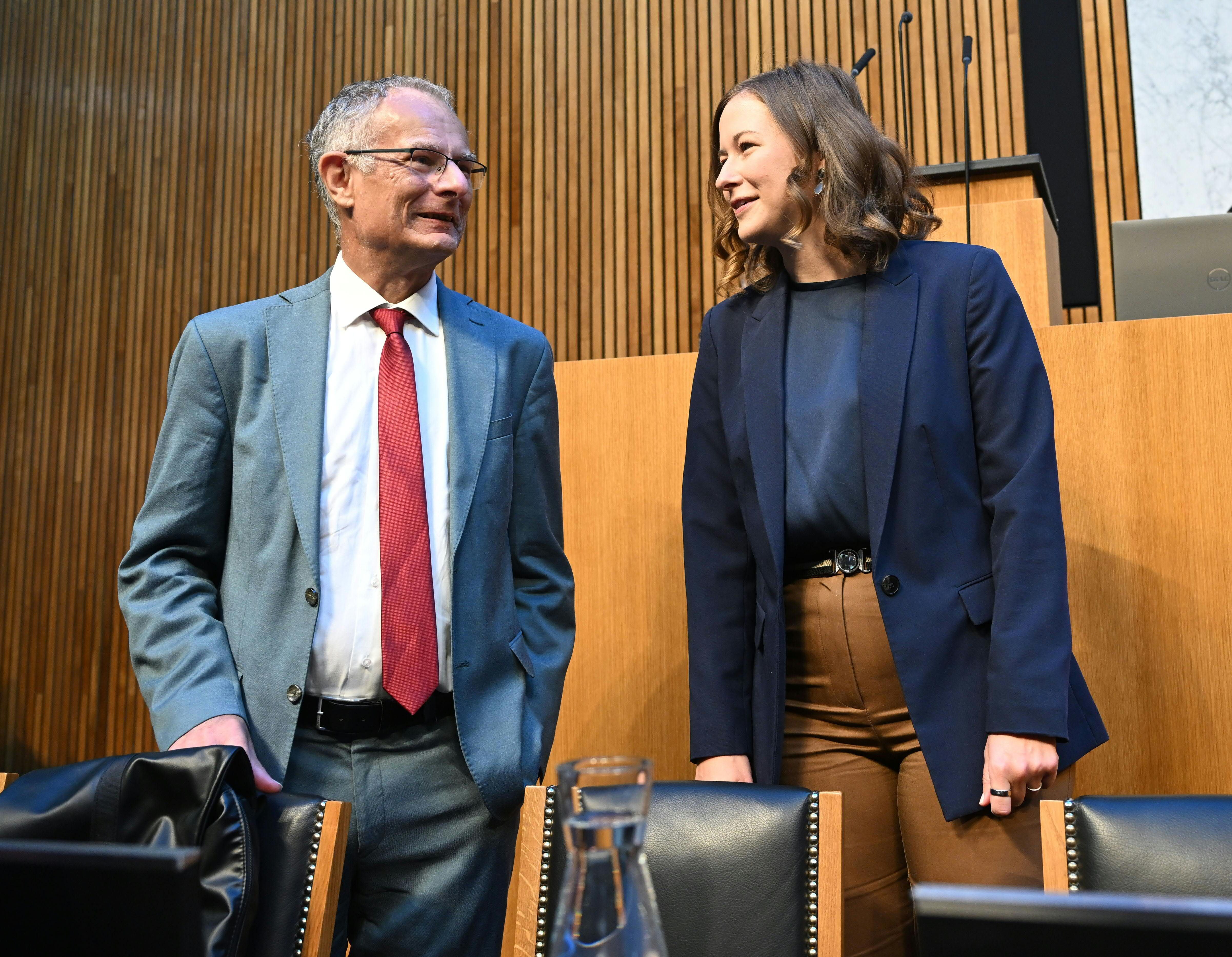 Zwei Personen im Anzug unterhalten sich in einem Sitzungssaal mit Holzverkleidung.