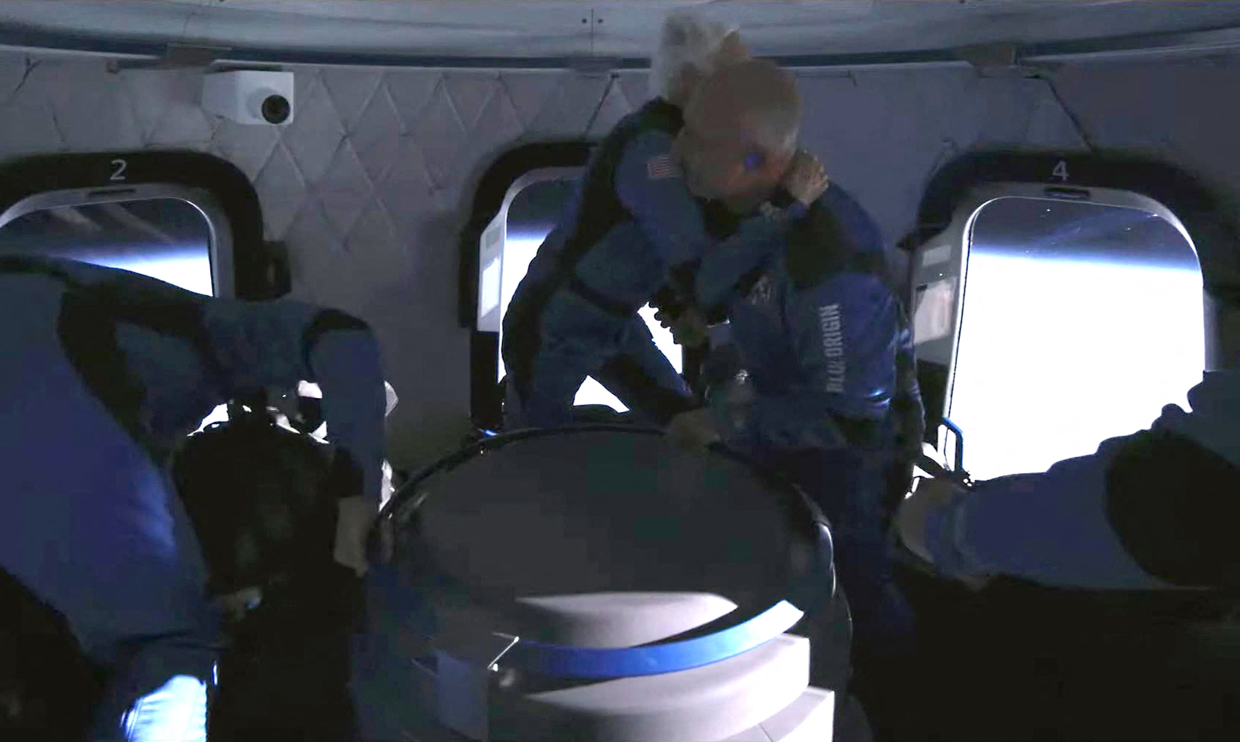 Menschen in blauen Raumanzügen umarmen sich schwerelos in einer Blue Origin Raumkapsel.