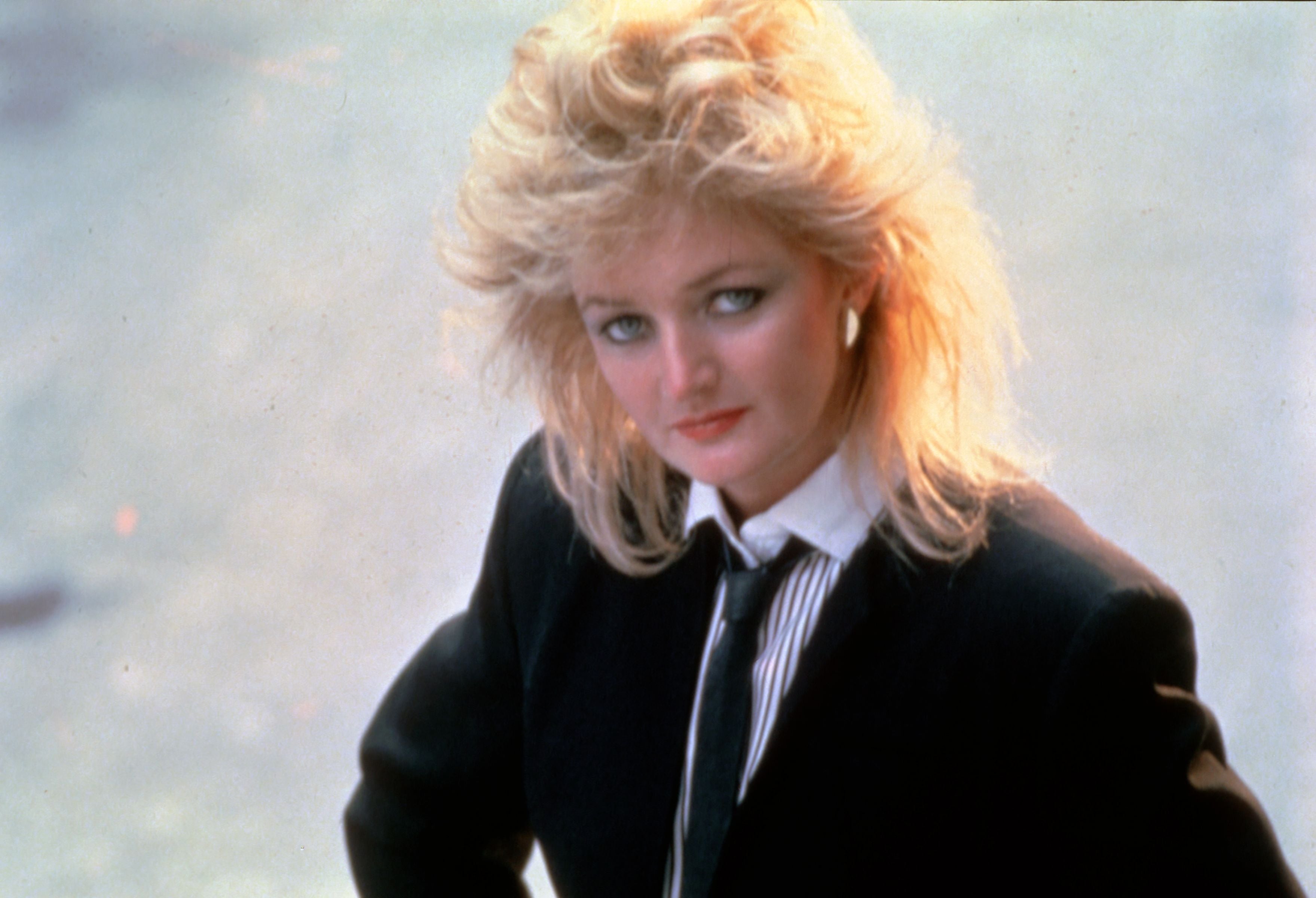 Frau mit blondem, voluminösem Haar im Anzug und Krawatte, 1980er-Jahre-Stil.