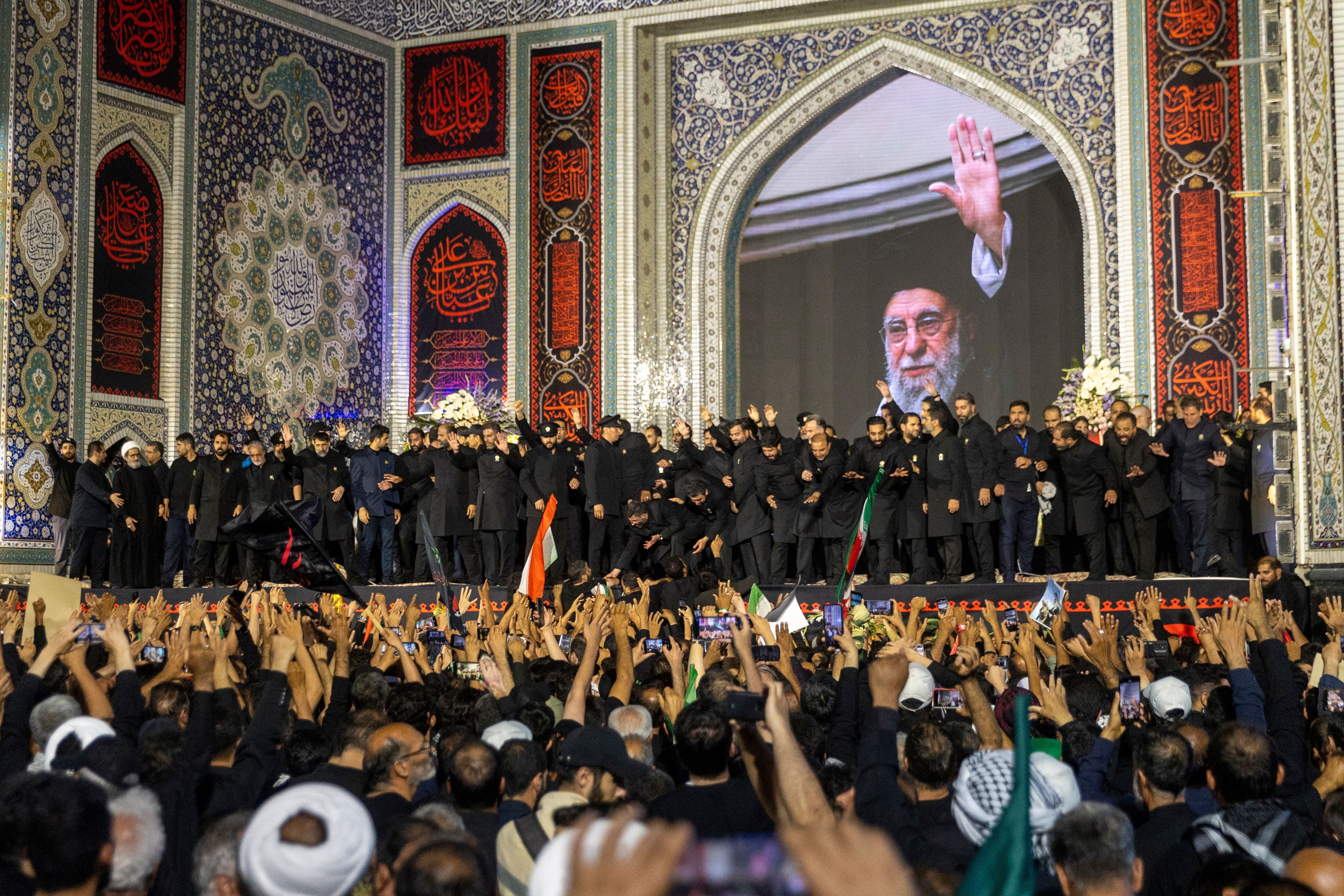 Menschenmenge bei einer Gedenkveranstaltung im Imam-Reza-Schrein mit großem Porträt im Hintergrund.