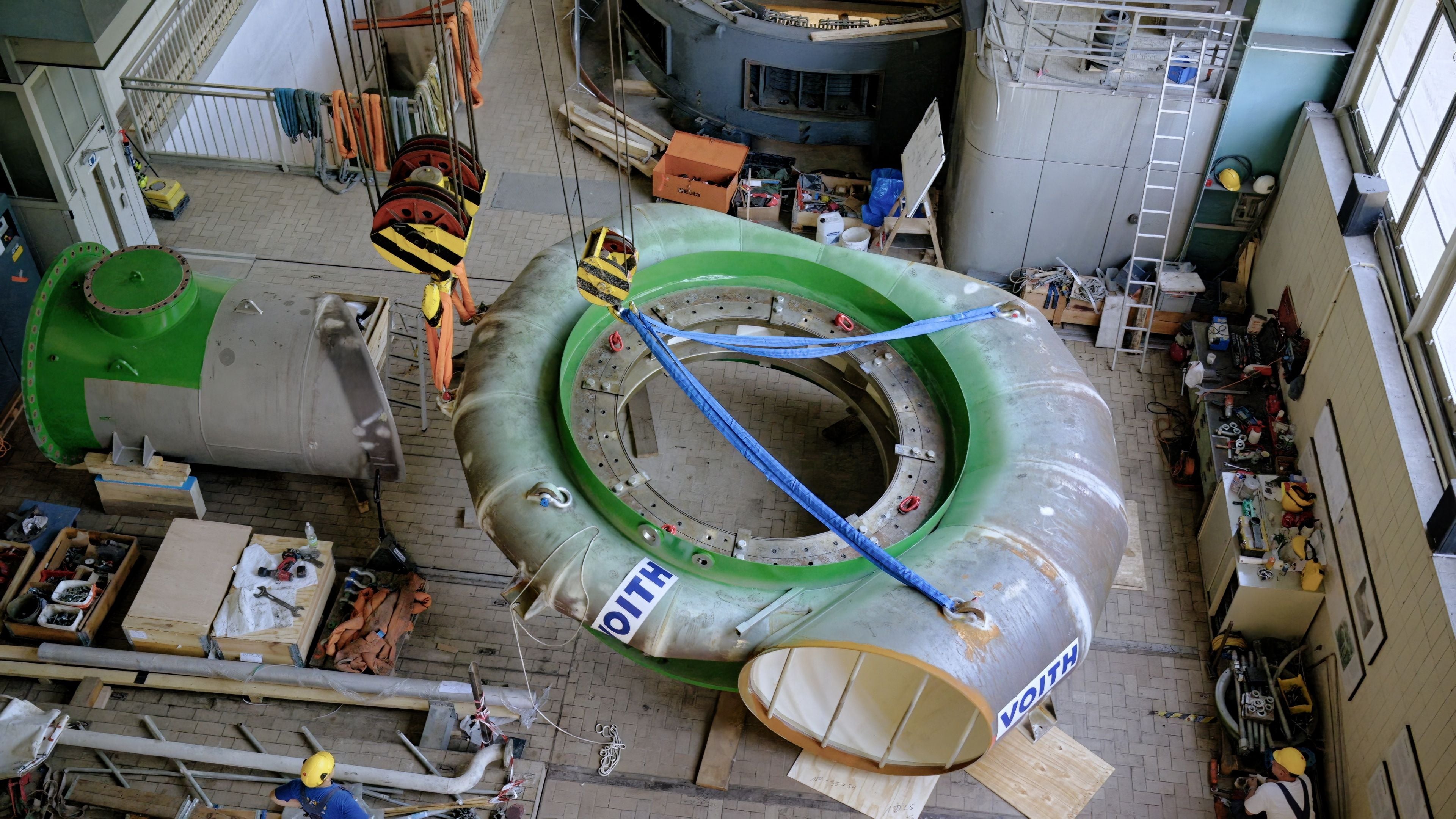 Große grün-silberne Pumpenspirale wird in einer Werkshalle mit Kränen montiert.