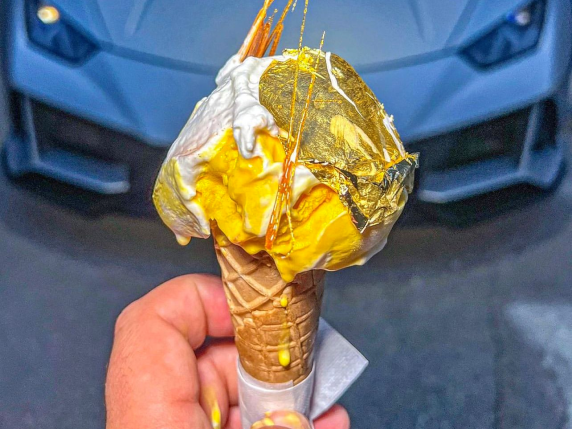 Eistüte mit goldener Blatt-Verzierung und gelbem Eis vor einem Auto.