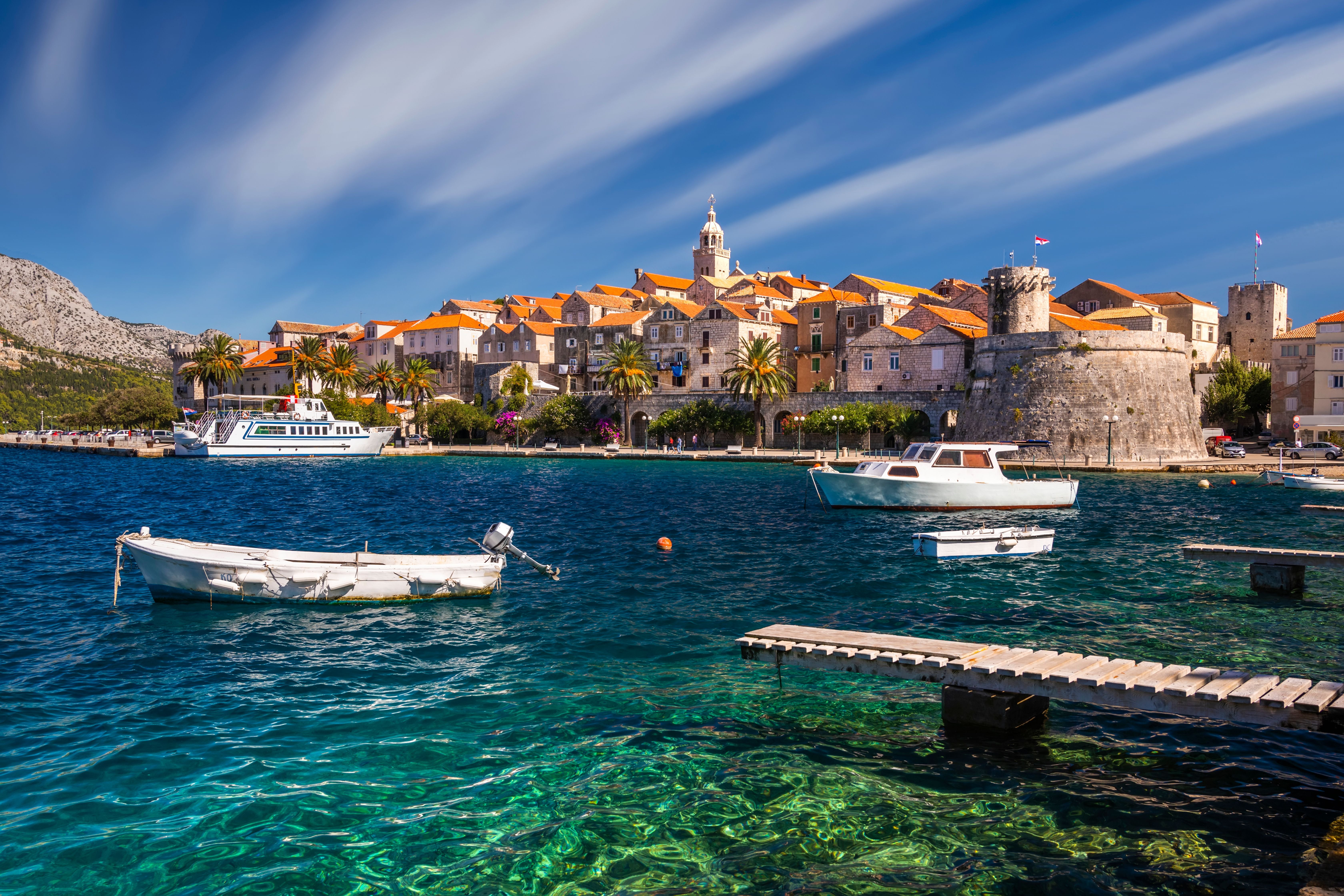 Boote auf klarem Wasser vor der historischen Altstadt von Korcula, Kroatien, bei sonnigem Wetter.