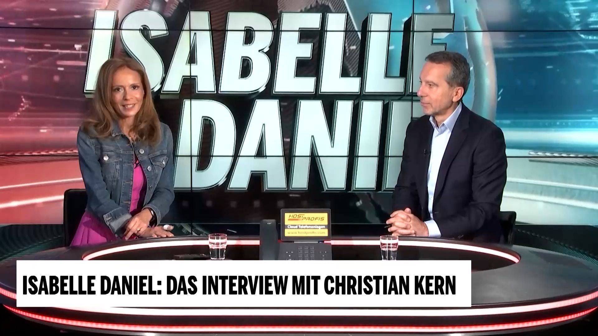 Zwei Personen sitzen im TV-Studio, Schriftzug „Isabelle Daniel“ im Hintergrund.