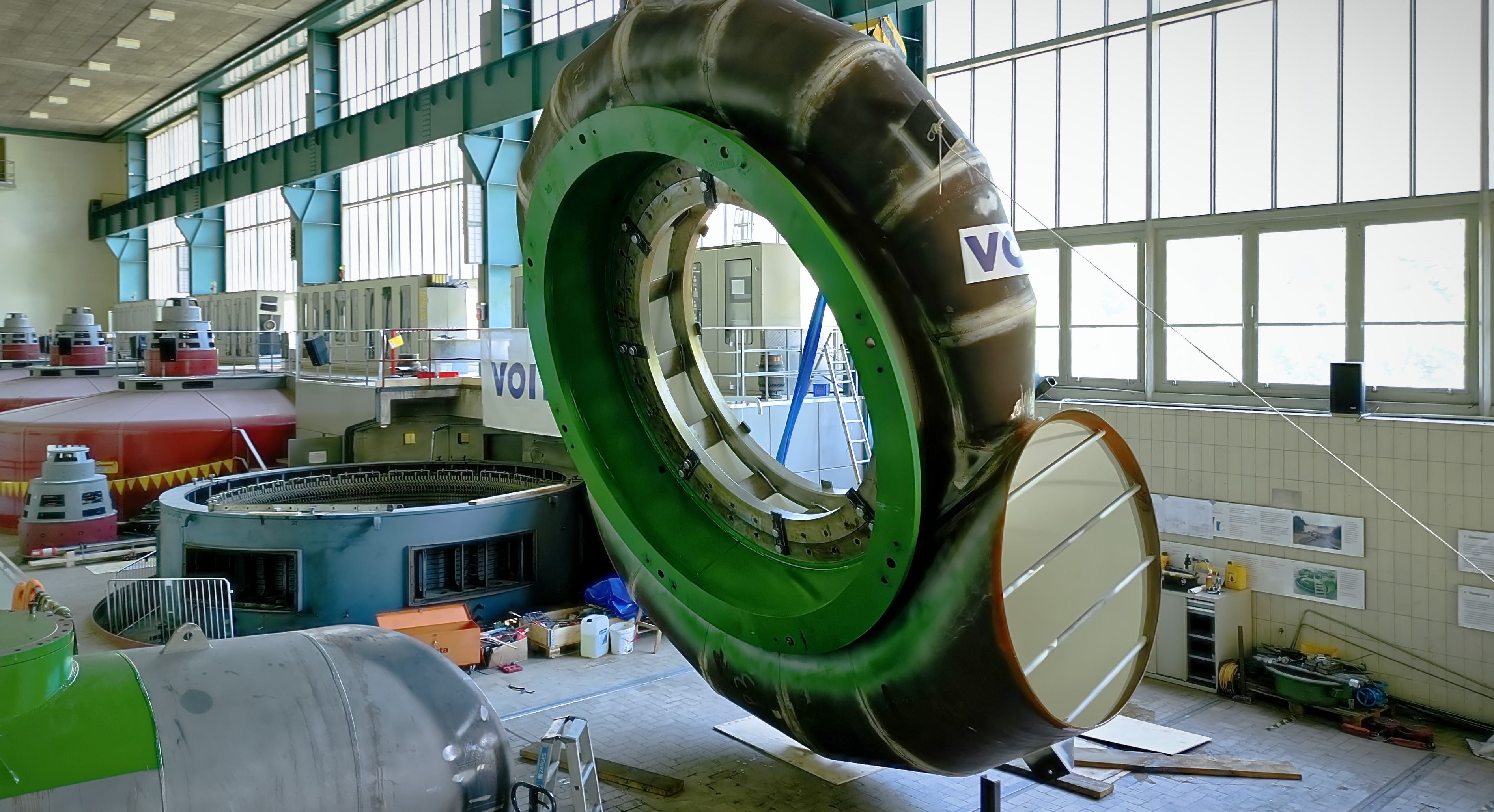 Große grüne Pumpenspirale in einer Fabrikhalle mit technischen Anlagen im Hintergrund.