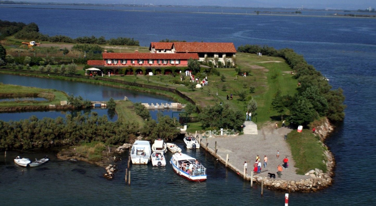 Insel Ravaiarina mit Restaurant, Steg, Booten und Menschen in der Lagune von Grado.