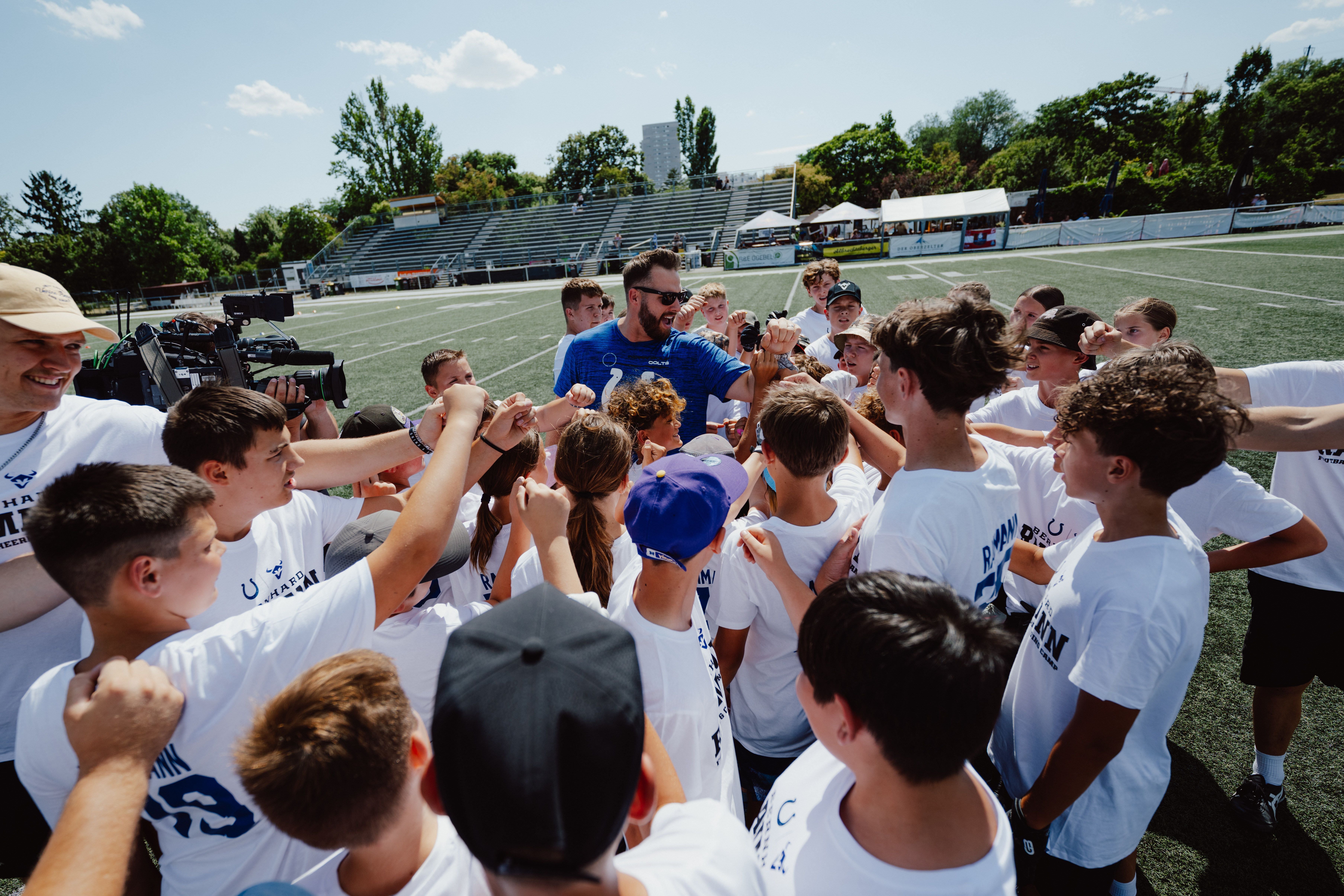 Eine Gruppe Kinder und ein Trainer jubeln gemeinsam auf einem Footballfeld.