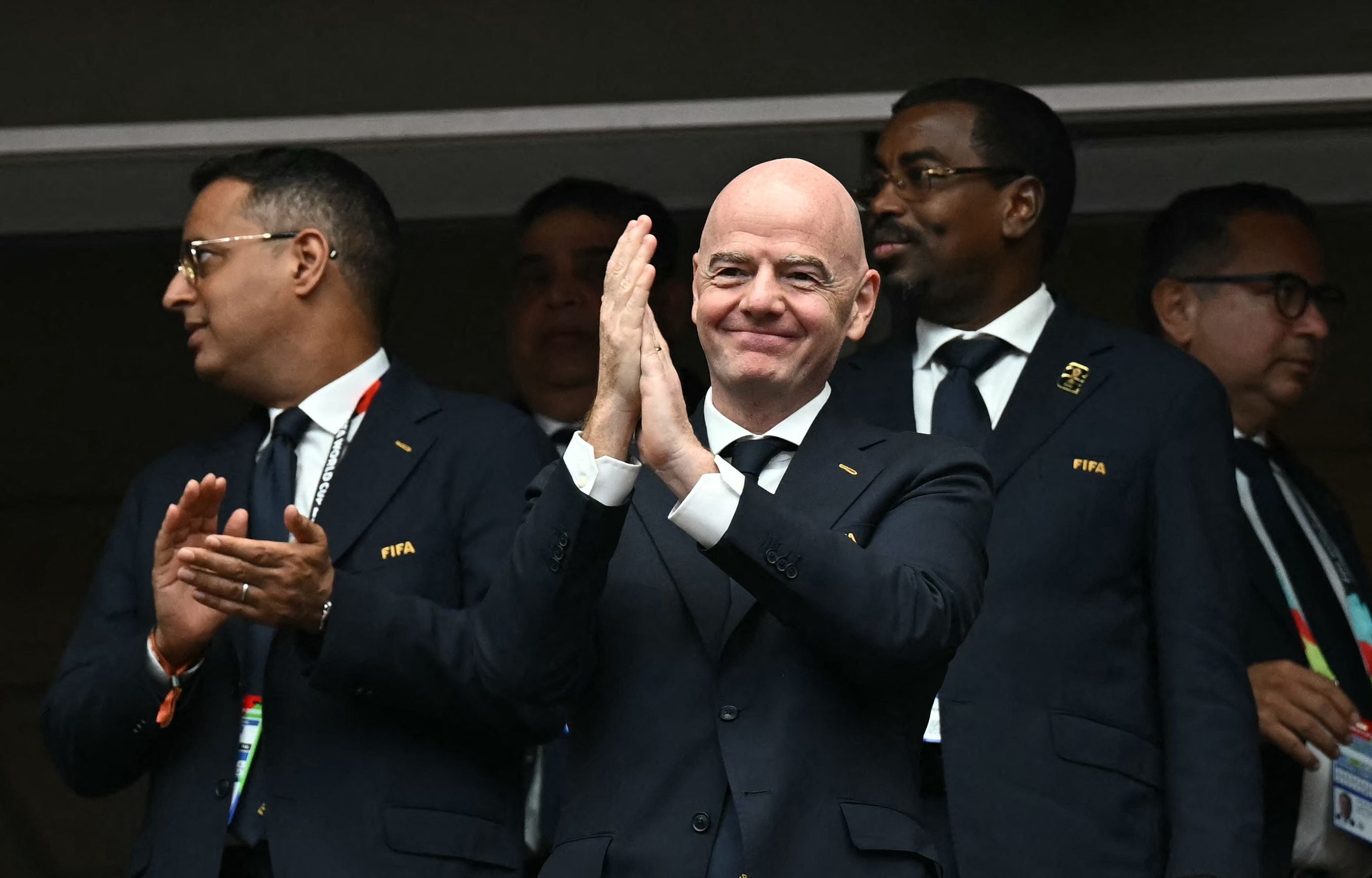 Mehrere Männer im Anzug mit FIFA-Emblem applaudieren in einem Stadion.
