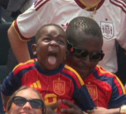 Ein Kind mit Spanien-Trikot streckt die Zunge heraus, ein Erwachsener hält es fest.