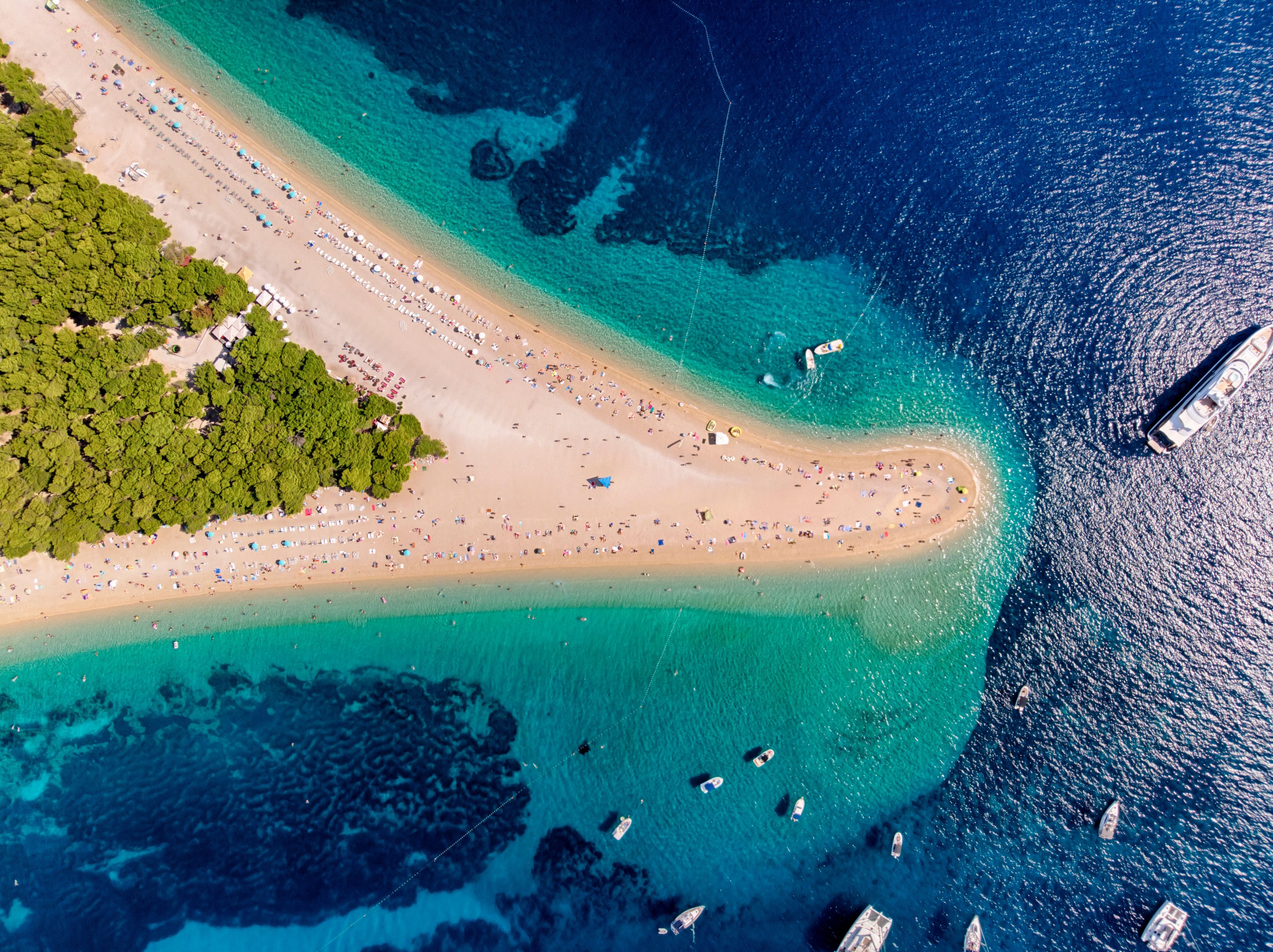 Luftaufnahme des Zlatni Rat Strandes mit türkisfarbenem Wasser und zahlreichen Booten.
