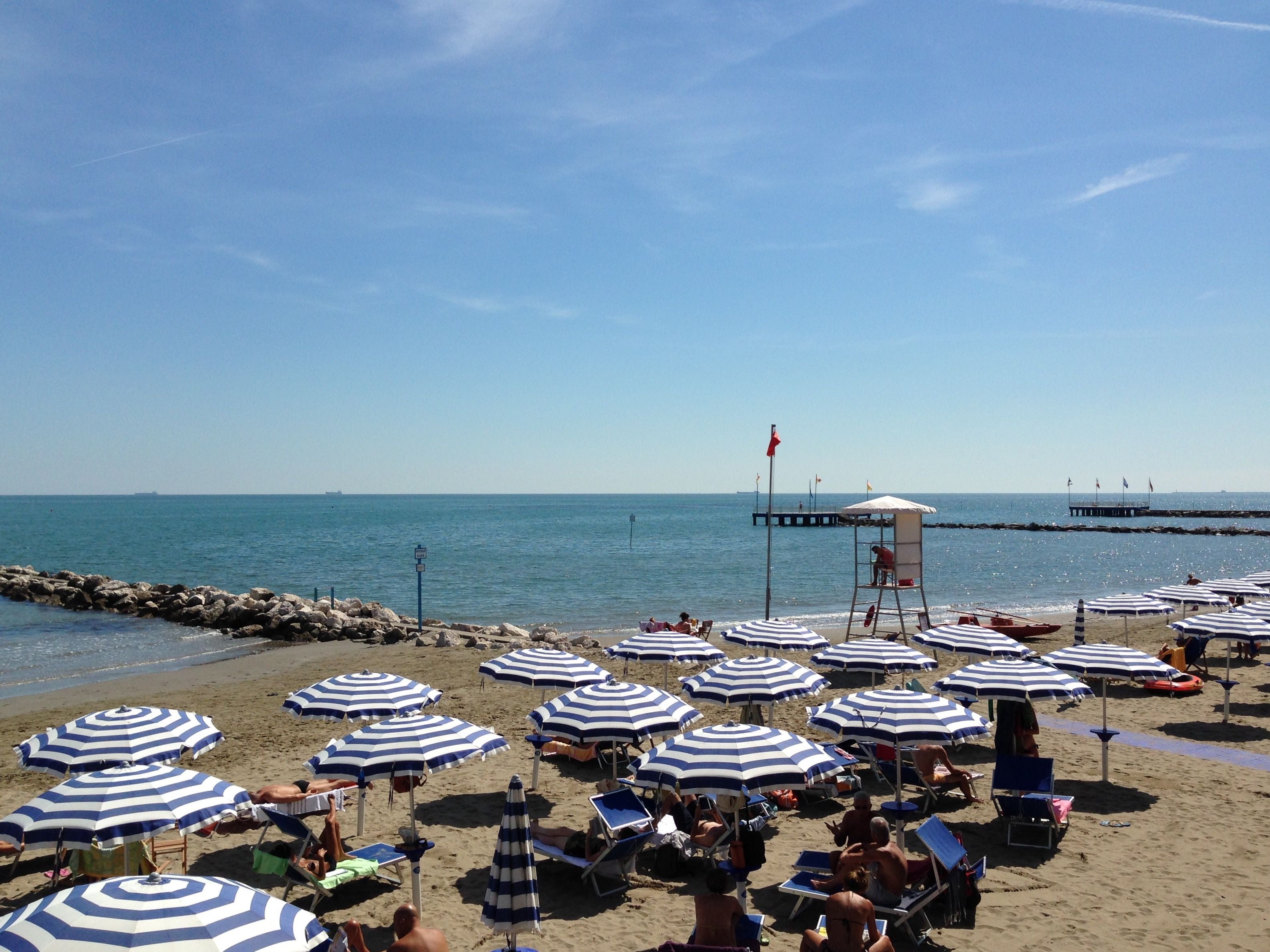 Strand mit vielen weiß-blau gestreiften Sonnenschirmen und einem Rettungsschwimmer-Turm.