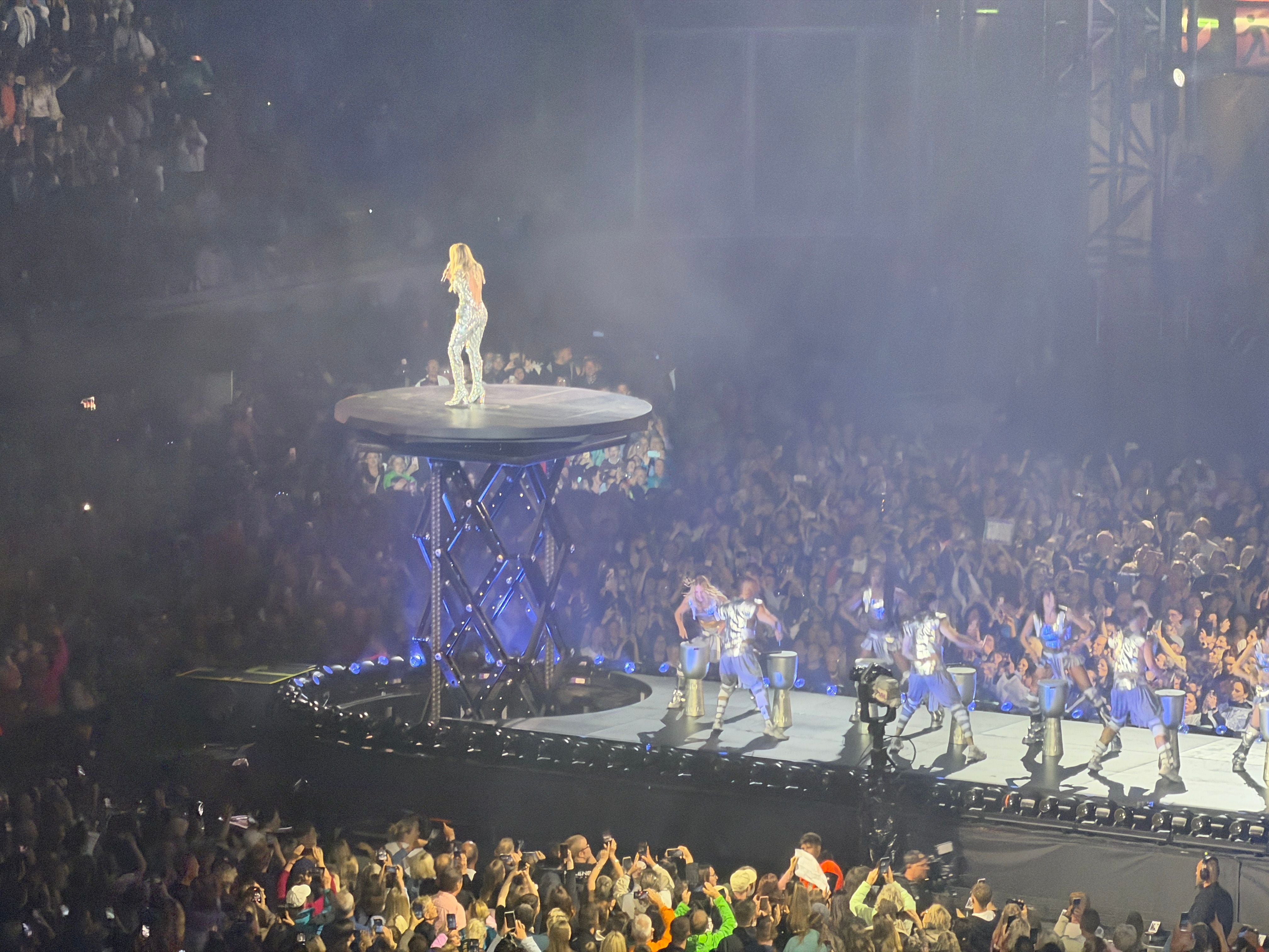 Sängerin auf erhobener Bühne mit Tänzern und Publikum bei einem Konzert in einer Arena.
