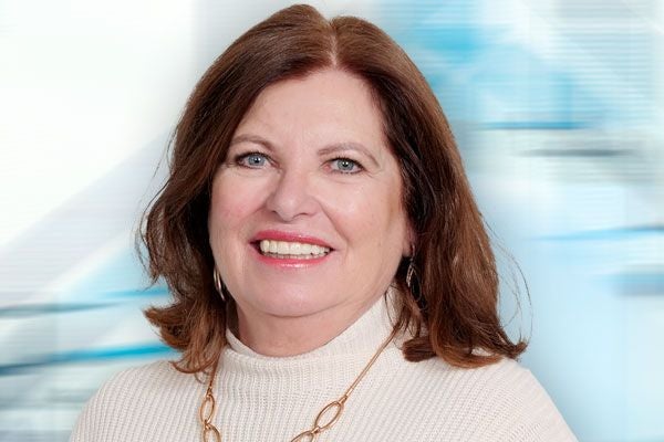 Frau mit braunen Haaren und hellem Rollkragenpullover lächelt in die Kamera.