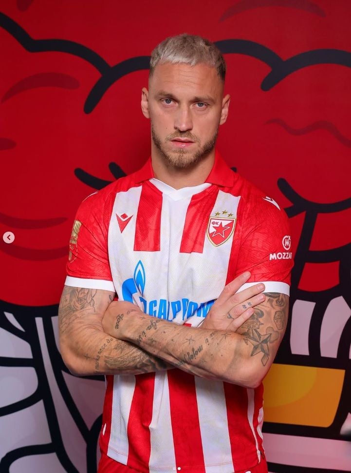 Ein Mann im rot-weiß gestreiften Fußballtrikot von Roter Stern Belgrad steht mit verschränkten Armen.