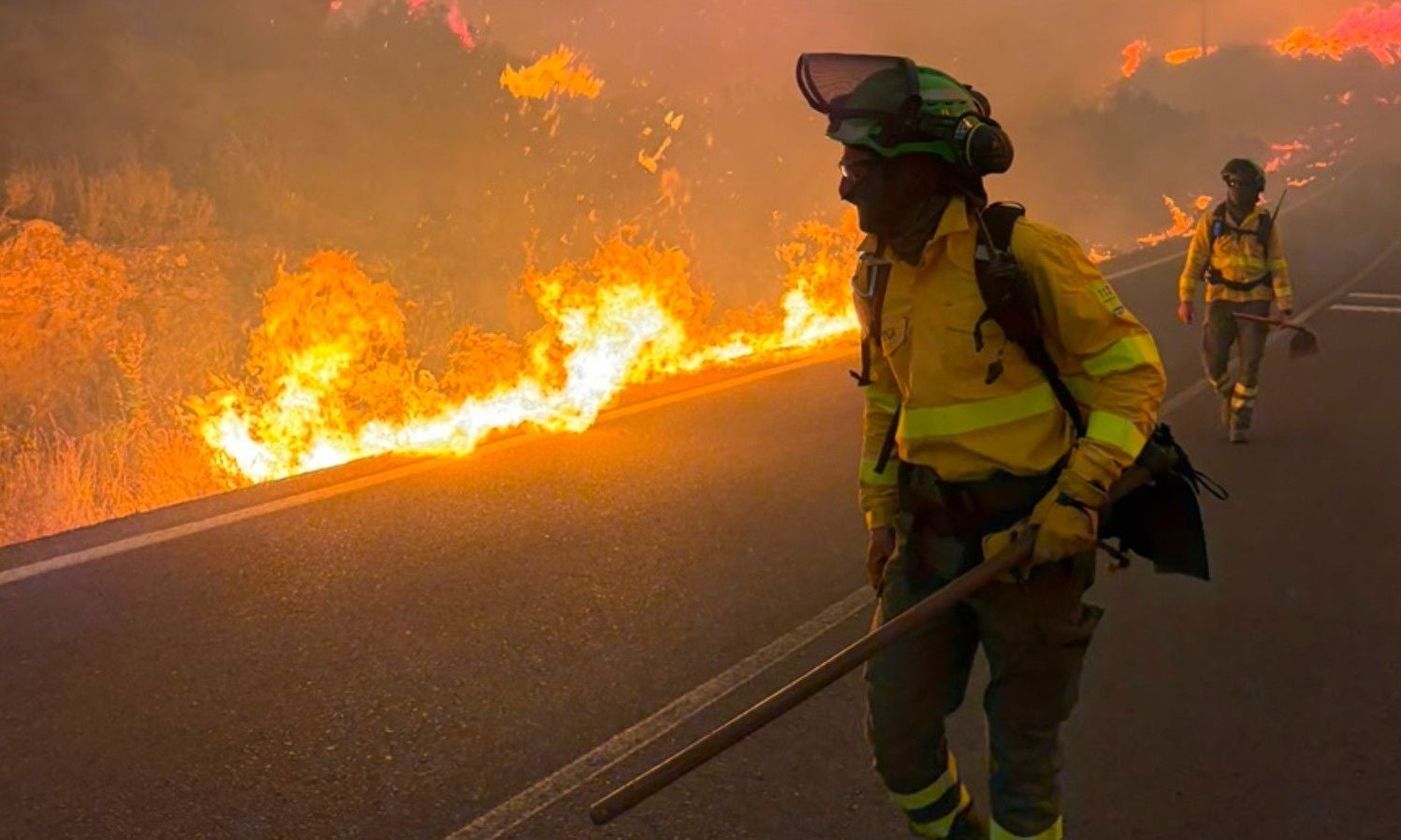 Feuerwehrleute bekämpfen einen Waldbrand neben einer Straße in Spanien.