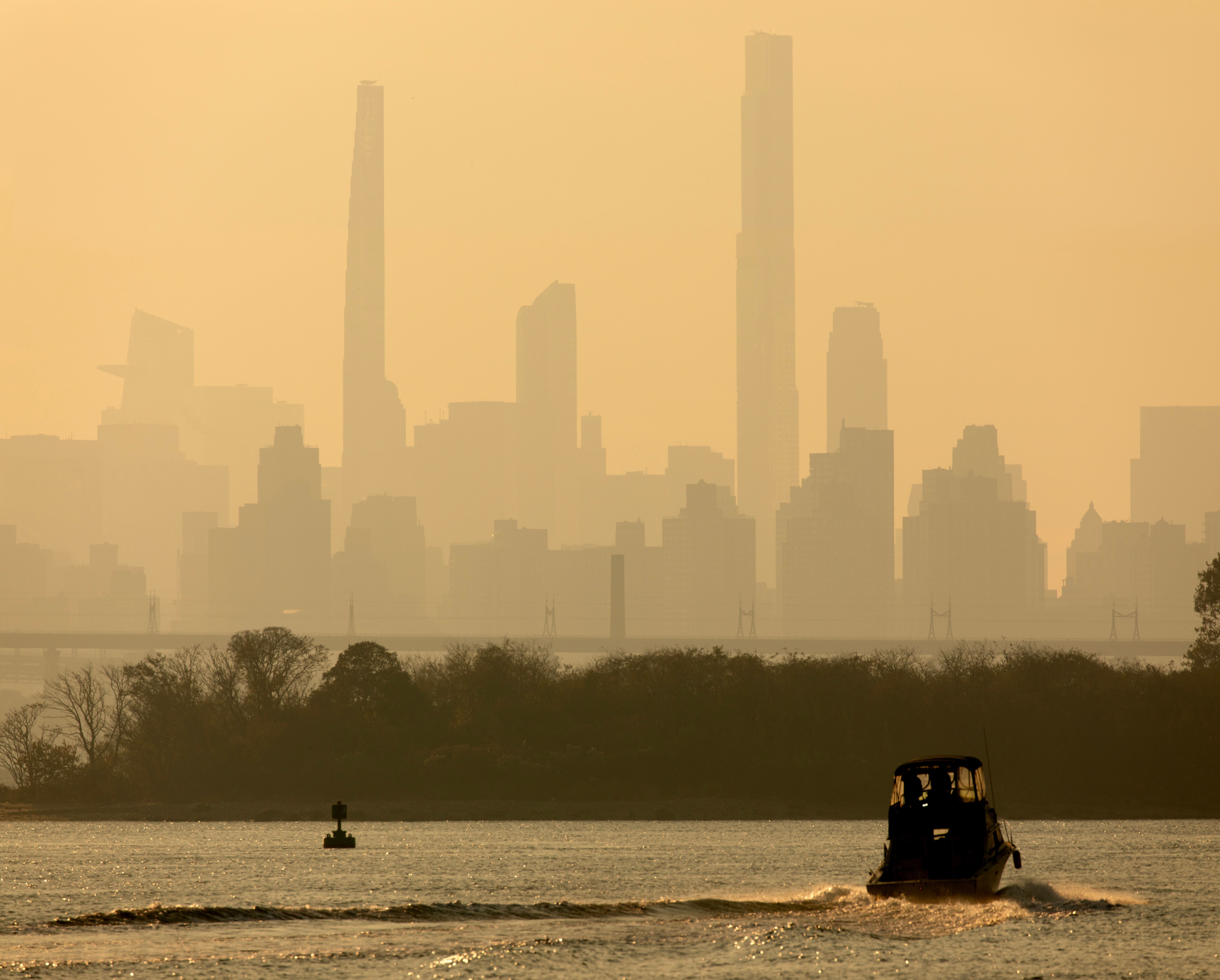 Kleines Boot fährt bei Sonnenuntergang auf dem Fluss vor der Skyline von New York City.