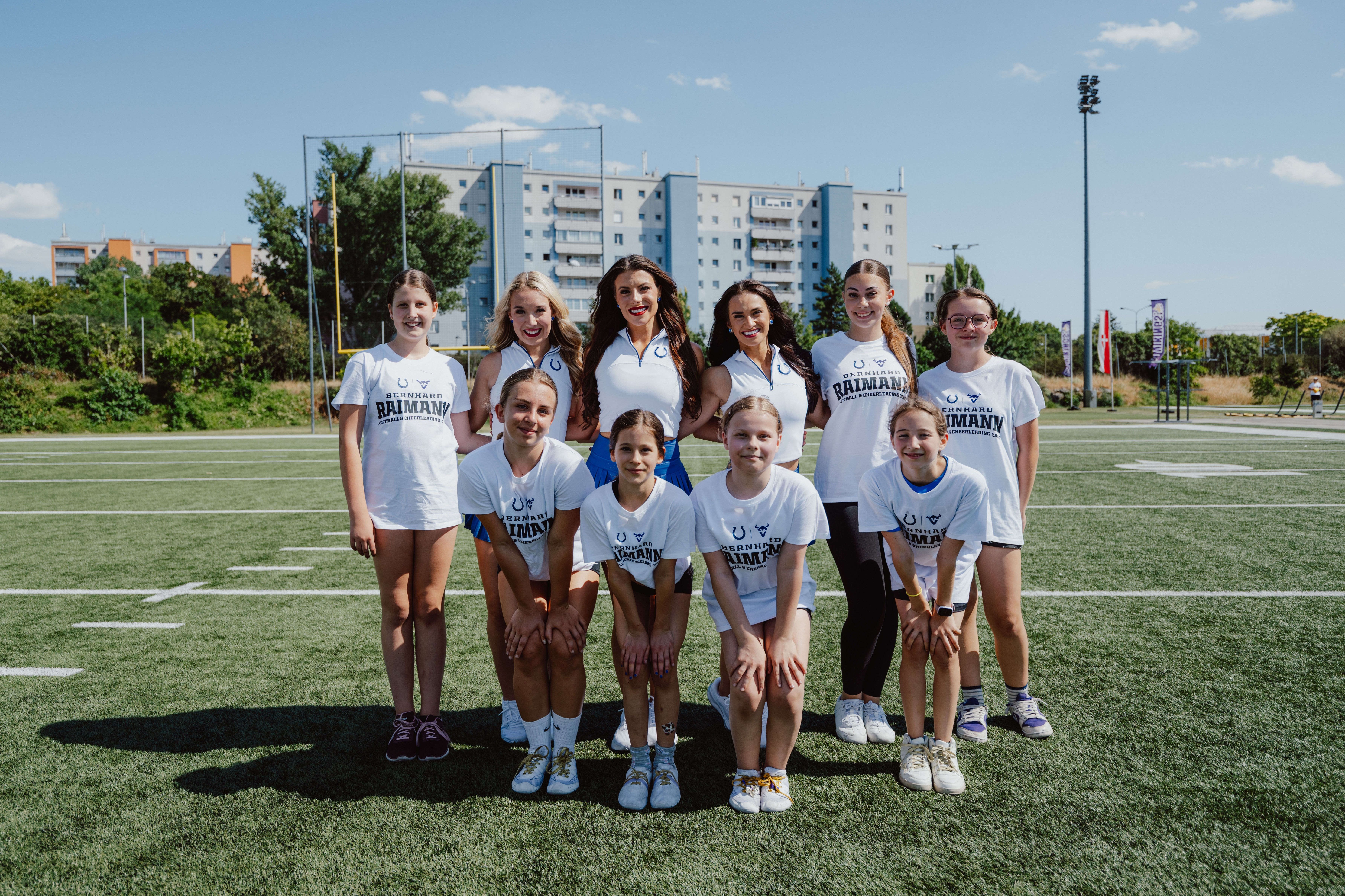 Eine Gruppe junger Cheerleader steht auf einem Footballfeld und lächelt in die Kamera.