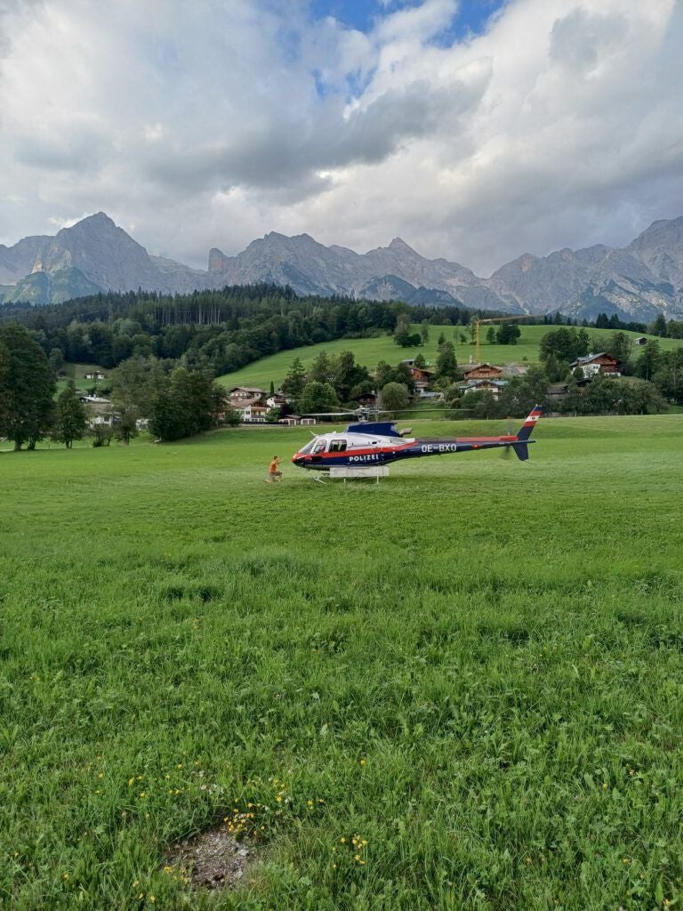 Ein Polizeihubschrauber steht auf einer Wiese vor Bergkulisse, eine Person geht darauf zu.