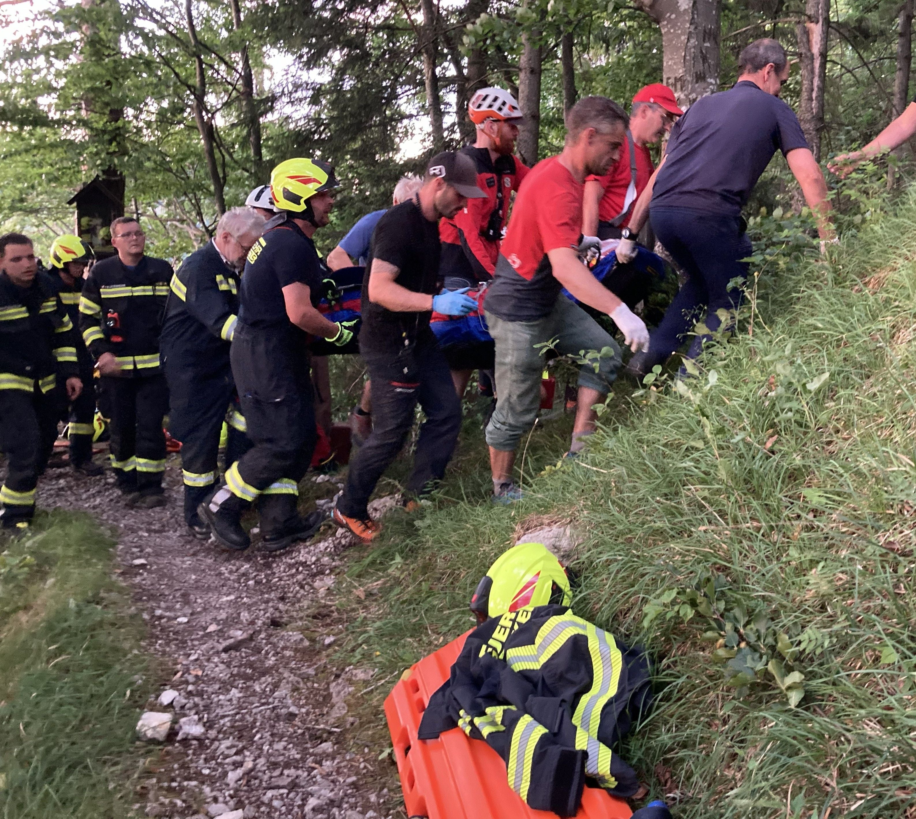 Rettungskräfte tragen eine verletzte Person auf einer Trage durch bewaldetes Gelände.