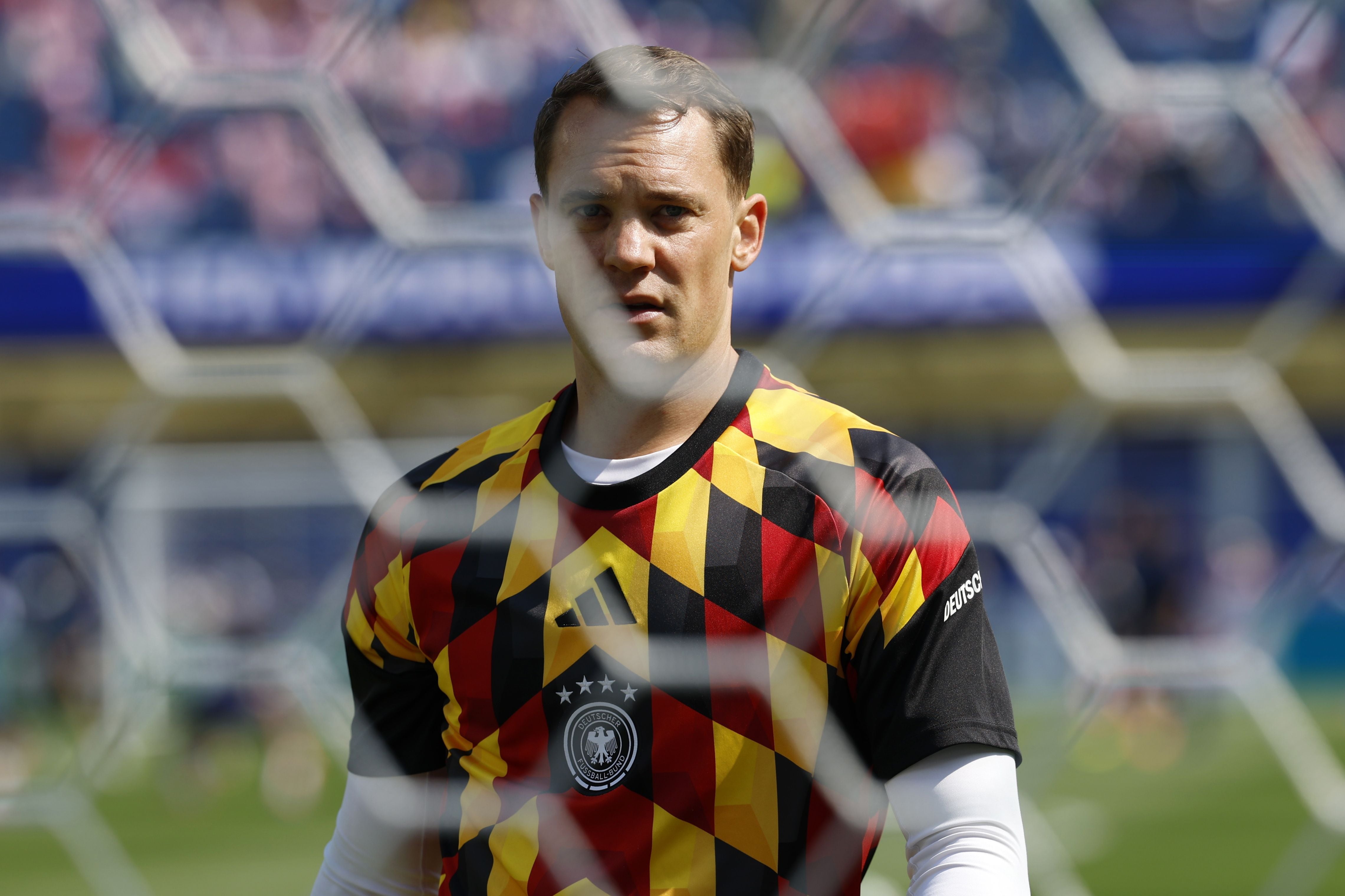 Ein Fußballtorwart im bunten Trikot wärmt sich vor dem Spiel im Stadion auf, das Tornetz im Vordergrund.