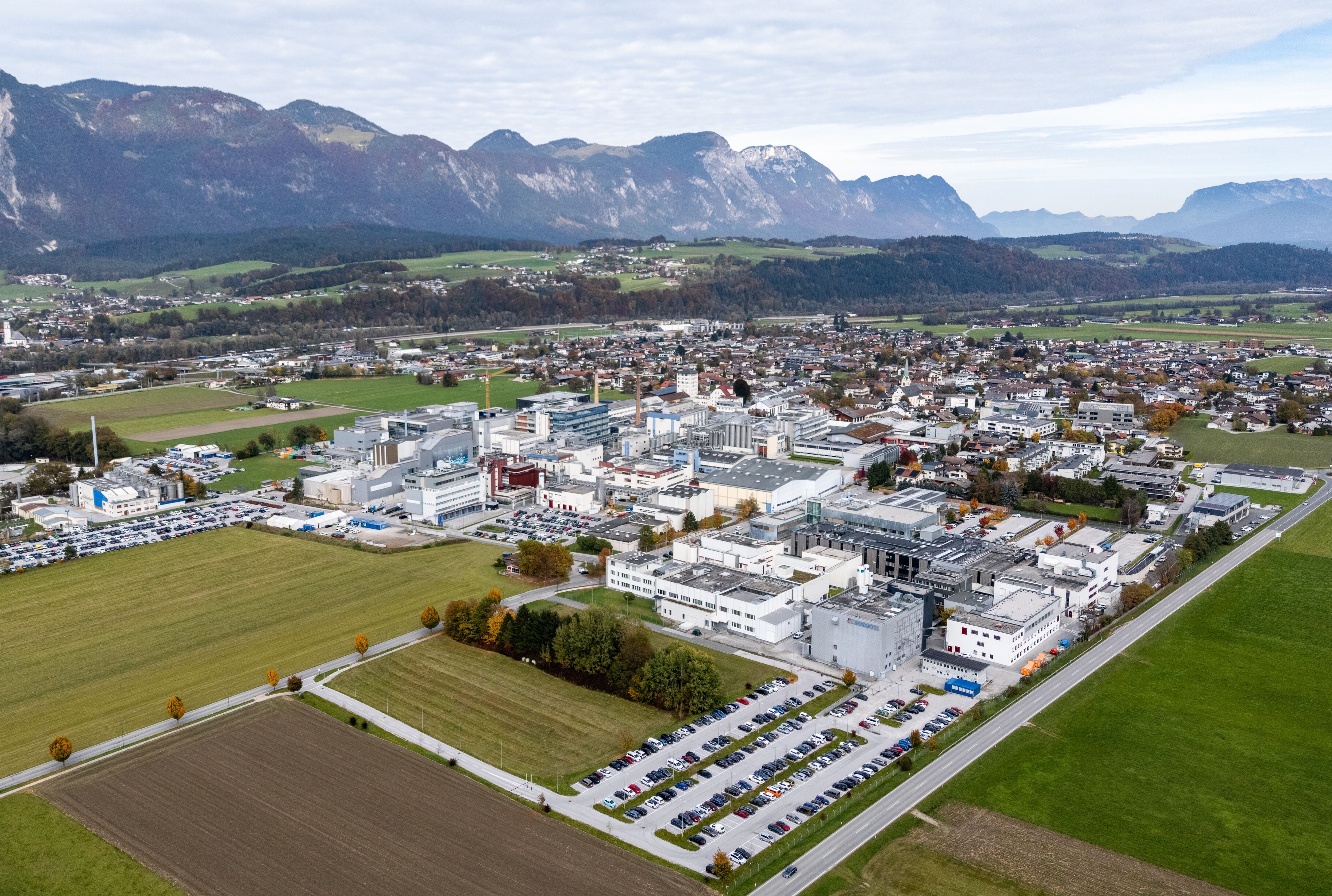 Luftaufnahme des Novartis-Betriebsgeländes in Kundl mit umliegenden Feldern und Bergen im Hintergrund.