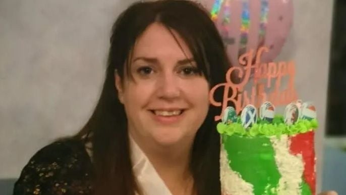 Frau lächelt hinter einer bunt verzierten Geburtstagstorte mit „Happy Birthday“-Dekoration.