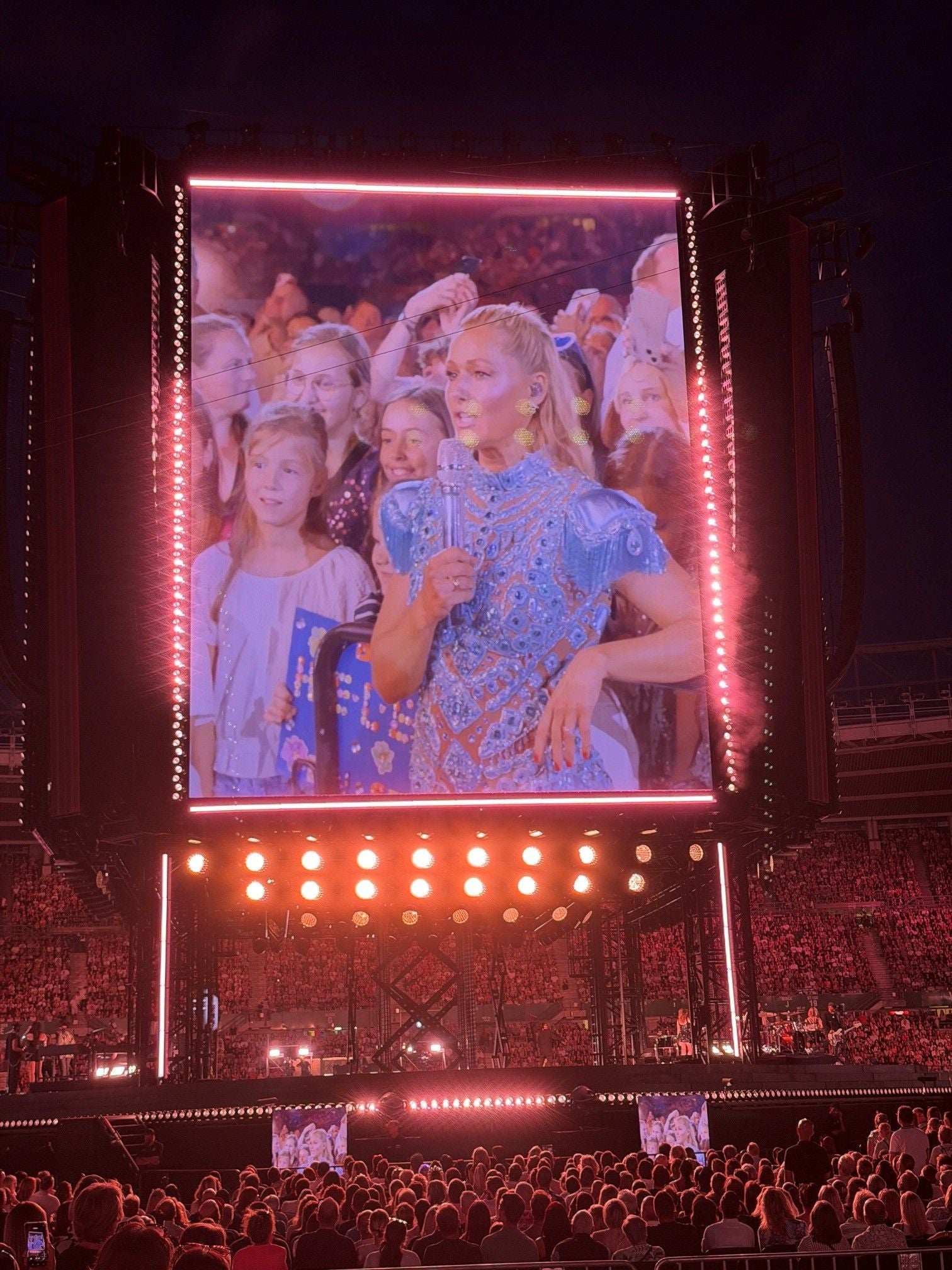 Großbildschirm bei einem Konzert mit einer Sängerin im blauen Kleid und jubelndem Publikum.