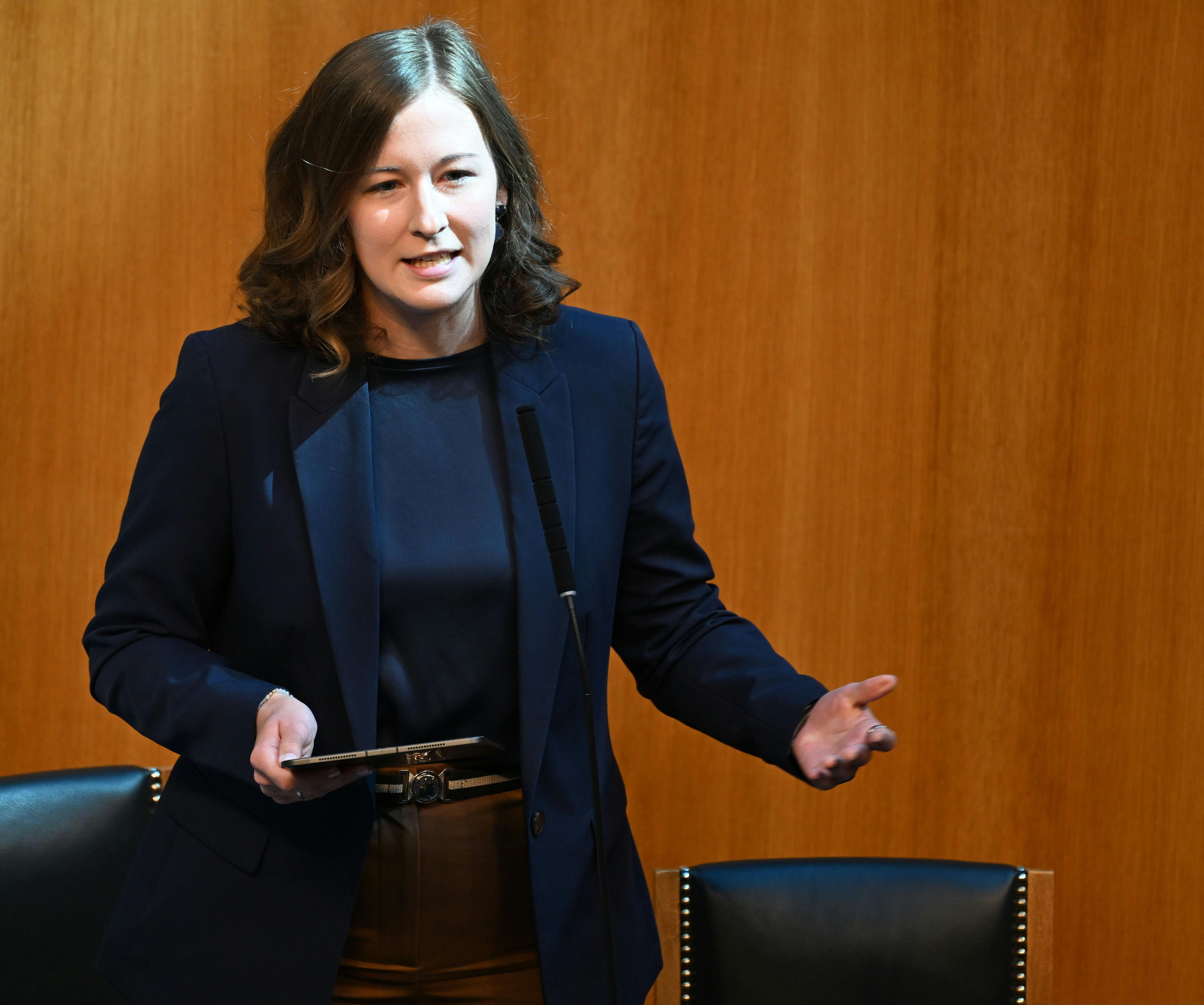 Frau spricht während einer Sitzung am Rednerpult im Parlament vor Holzvertäfelung.