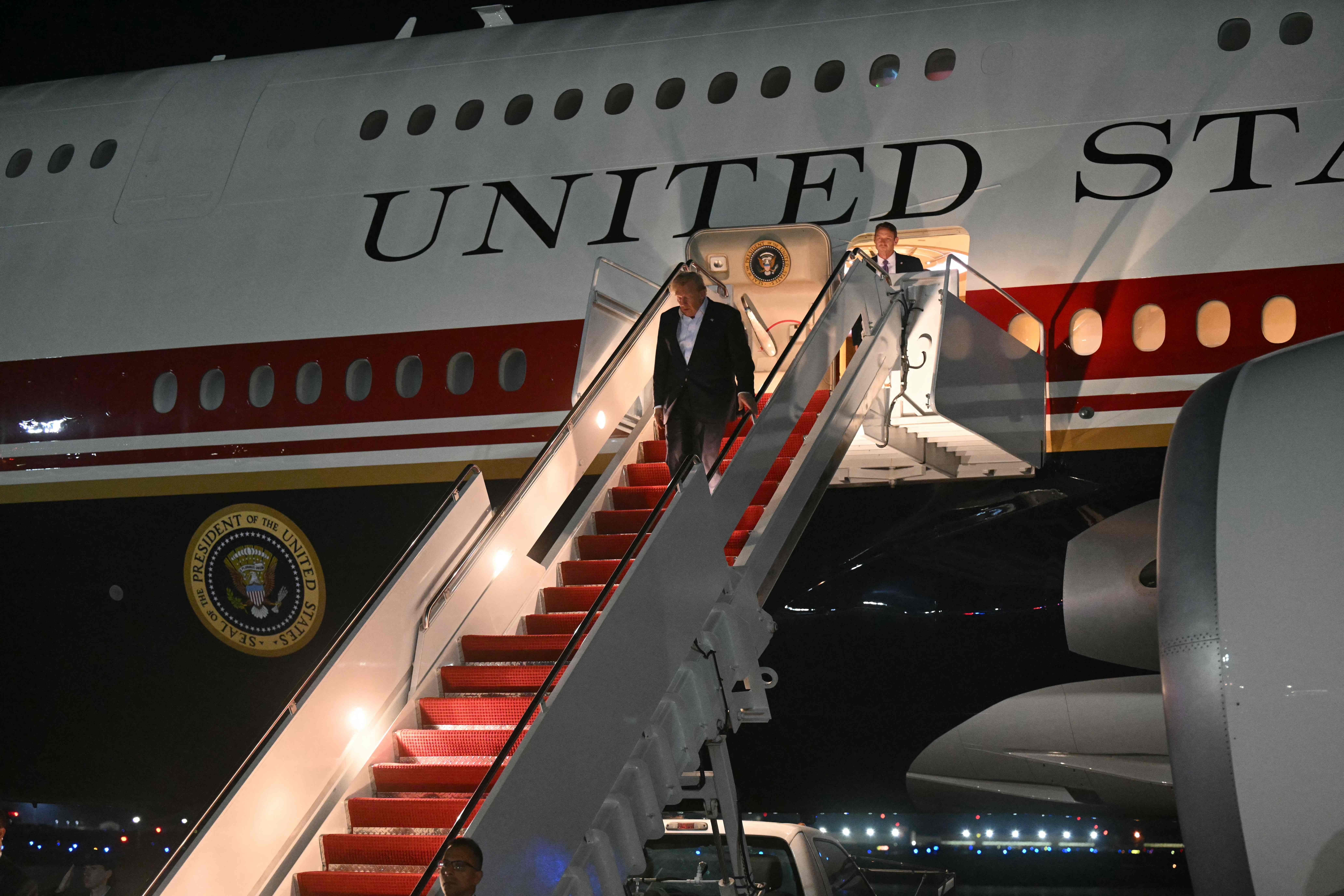 Donald Trump steigt nachts aus der Air Force One auf einer beleuchteten Flugzeugtreppe aus.