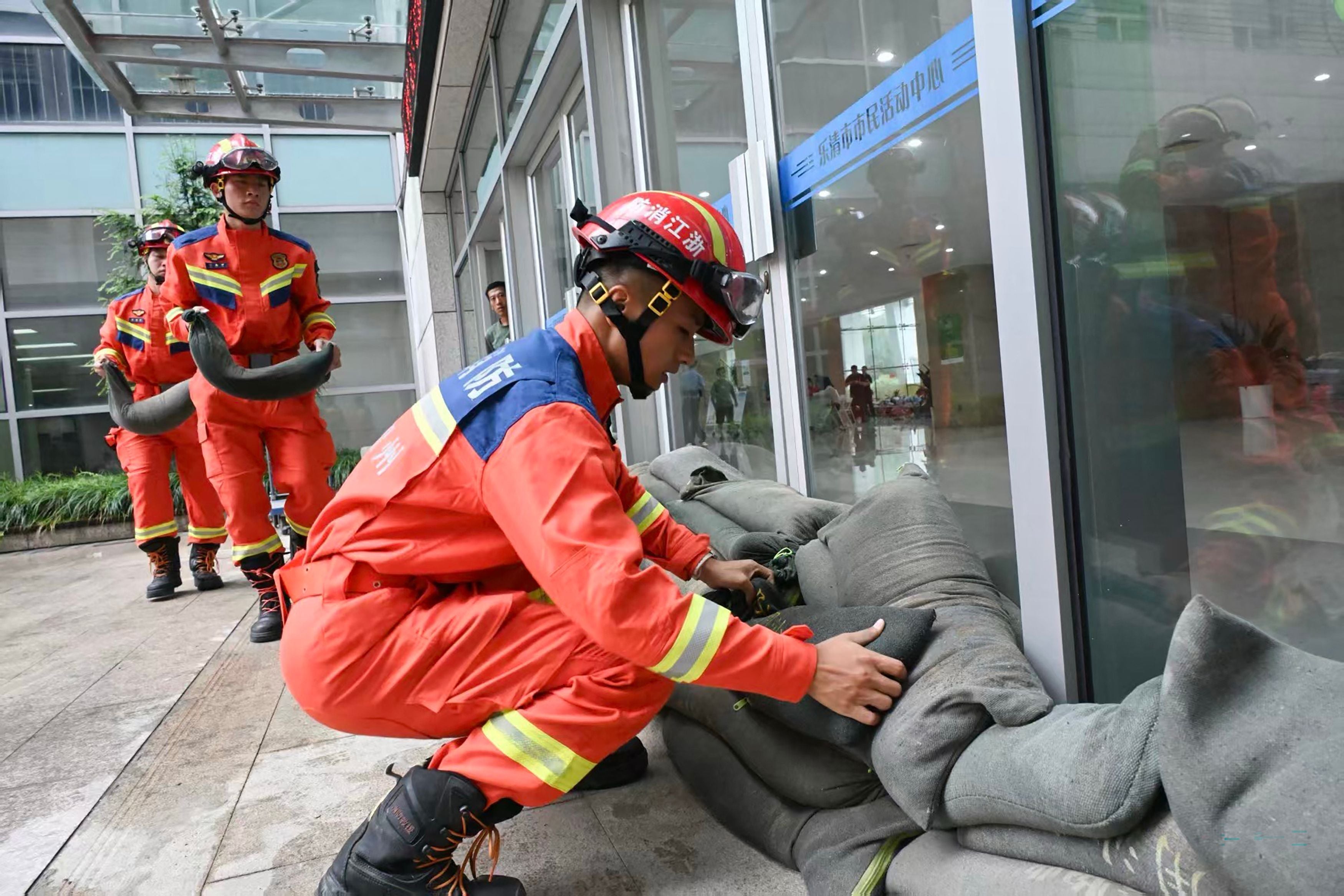 Feuerwehrleute stapeln Sandsäcke vor Fenstern eines Evakuierungszentrums in China.