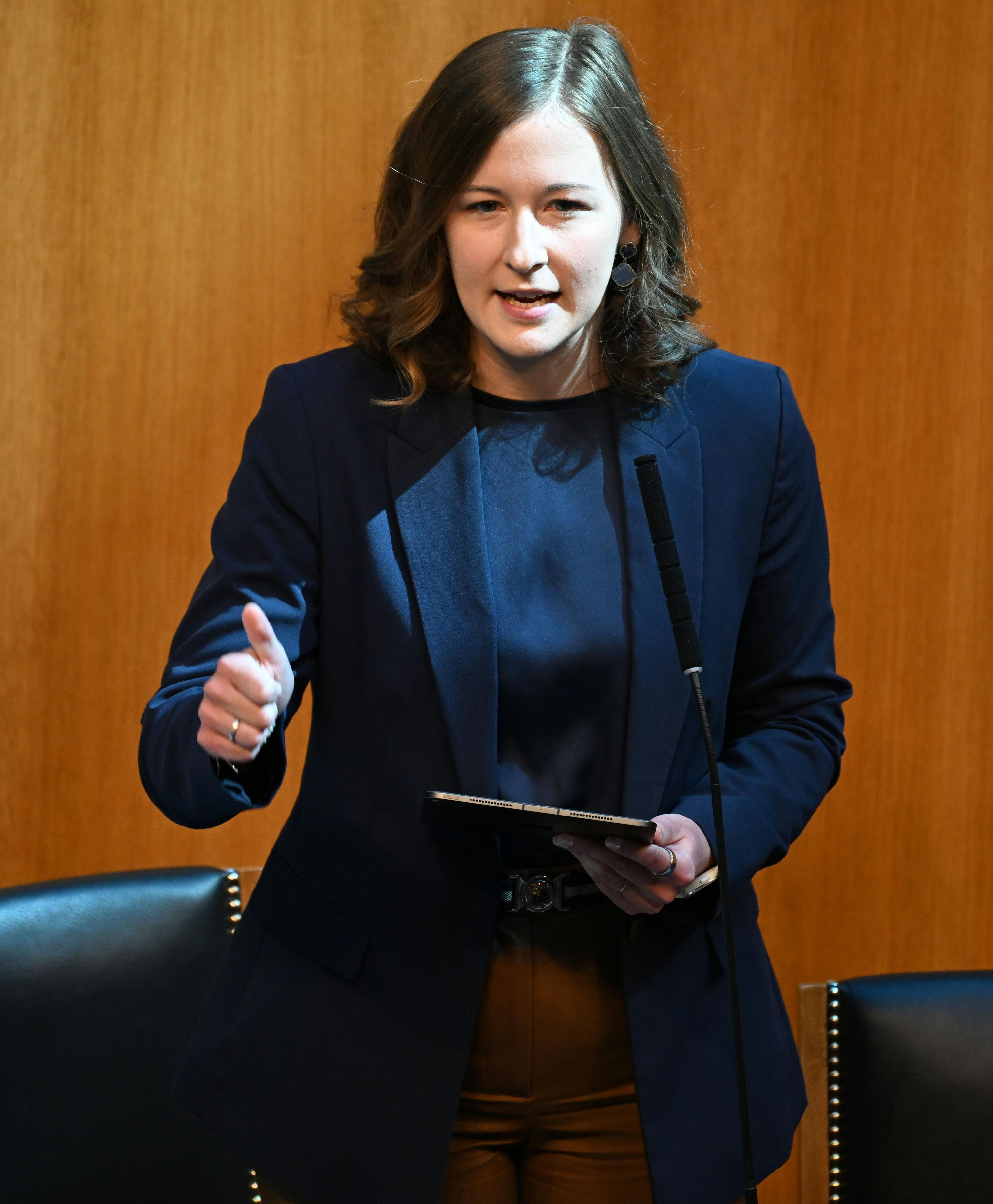 Eine Frau spricht im Parlament an einem Mikrofon und hält ein Tablet in der Hand.