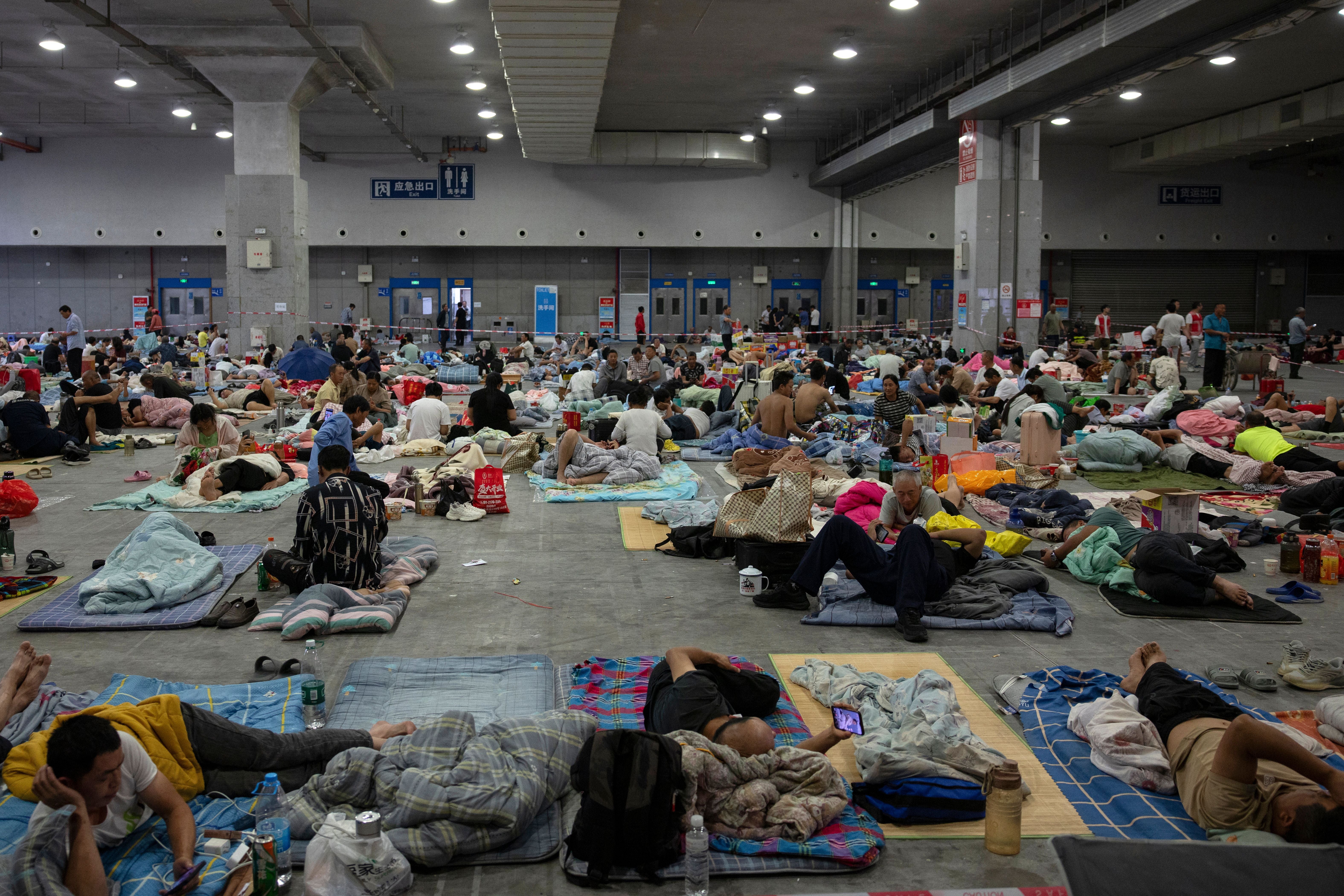 Viele Menschen ruhen auf Matten und Decken in einer Notunterkunft in einer großen Halle.