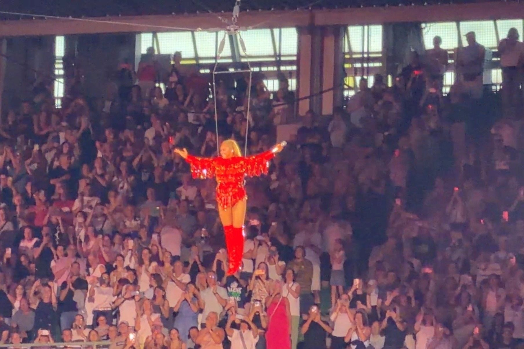 Helene Fischer schwebt bei einem Konzert in rotem Outfit über der jubelnden Menschenmenge.